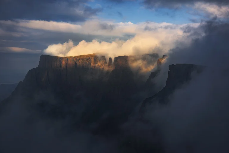 Through the heavy mist light falls, a view so epic and breathtaking, a moment in which you feel so alive and one worthy of those hours slogging up a mountain to get to this view. The mist closed in moments after this photograph was taken, and the opportunity of sunset was over. This momentary glimpse was all I needed to capture the true essence of the Drakensberg mountains.