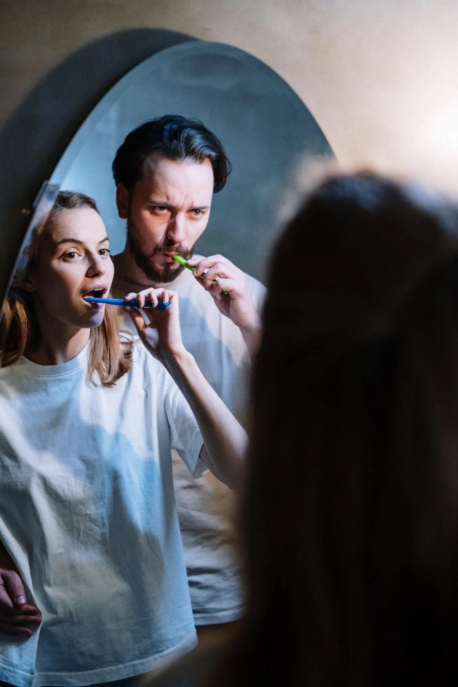 married couple brushing teeth in mirror