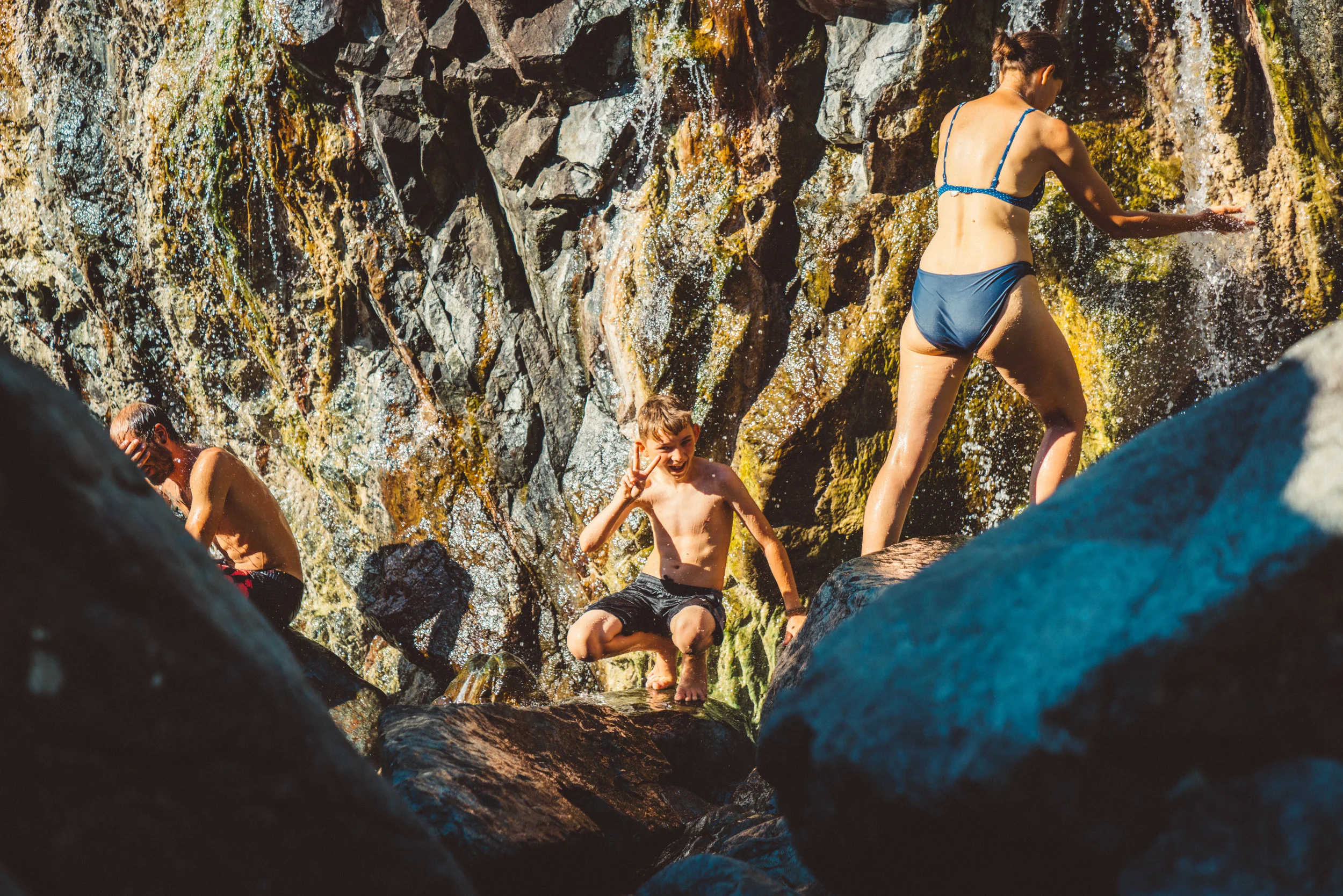A stranger, Trissy's son, Jude, and Trissy under the warm waterfall.