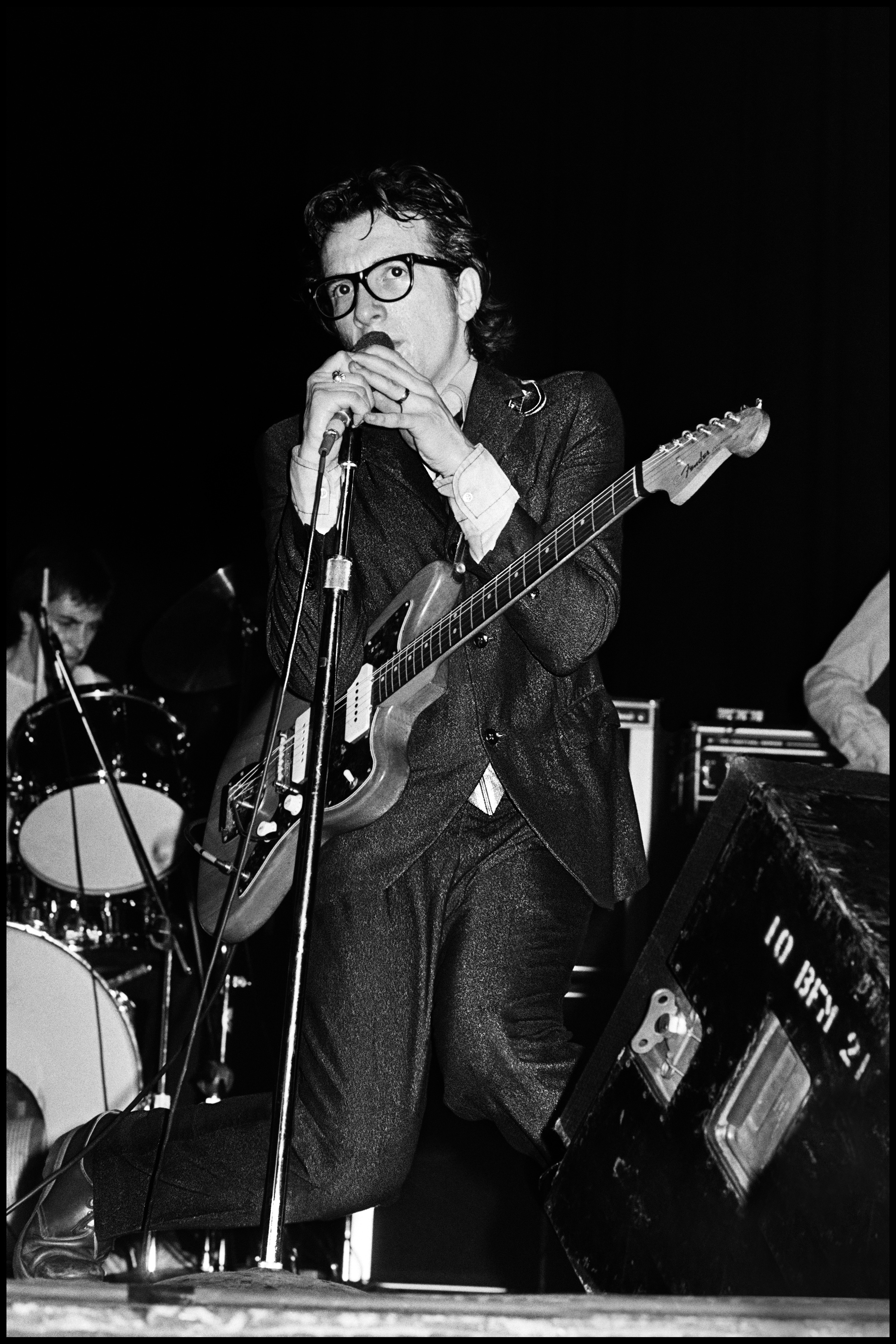 Elvis Costello at The El Mocambo - Toronto 1978 My philosophy regarding live photography was simple, instead of wasting film, study the show on the first night, see where the best opportunities occur, then concentrate on getting the best photographs during those numbers the following night. Given that Elvis was playing the El Mocambo, a small club in Toronto,it meant using flash, and that meant taking as few pictures as possible. I saw that during Less than Zero and Watching the Detectives EC gave his most animated and manic performances. Not only that, he dropped to his knees in Detectives just after singing "she's painting her nails as they're dragging the lake" and my aim was true, it was to catch that particular moment. I waited patiently and caught him right on cue, I was mighty happy with myself, but his manager was not happy with me. Whilst accepting that Elvis did this every night Jake did not want the public to know, he wanted each audience to think it was spontaneous, so he told me quite bluntly that I could not use the photo. I reluctantly agreed, because I could see the logic behind this decision, it was strategic in nature and I respected that. Jake respected me for agreeing and from that day on gave me total access to EC whenever I needed it. So I waited thirty five years before making it available, to me it sums up those early years perfectly.