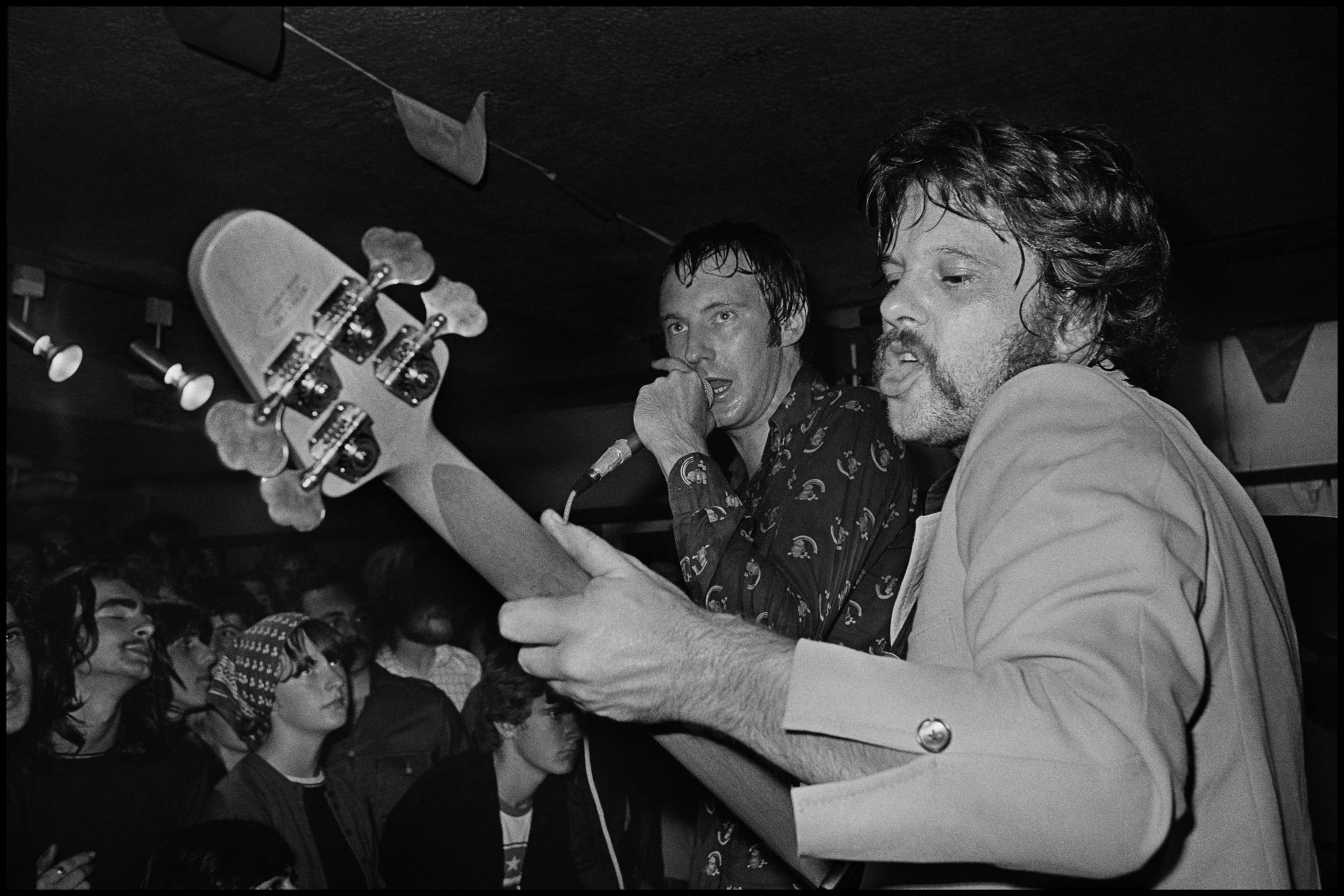 Dr Feelgood at the Hope and Anchor Benefit 1977 There was an unwritten rule about photographing live gigs, No Flash. But, there were times when you had no choice, especially in Clubs, Elvis Costello at the El Mocambo was another one. The bands don't like it because the strobe can phase them when they are not expecting it, the punters don't like it because it destroys the ambience a bit. So I used to do it very rarely, and when I did I picked my moments carefully. I knew the Feelgoods really well so they did not mind me standing on the side of the stage, but at the Hope and Anchor the stage was tiny, and the Feelgood's were a big band by now and even in this tiny club they had a huge PA, just look at the size of the monitor wedges. I was literally a couple of feet from Sparko when I took this photo, I only ever took a few frames, and once I knew I had something great I stopped. I think this shot really sums up the energy of their live act, Wilco is on the other side of the stage so I was unable to see him, but it's nice to have a big close up of Sparko and Lee in action. They were one of the best live bands ever, and this night was the best show I ever saw them play.
