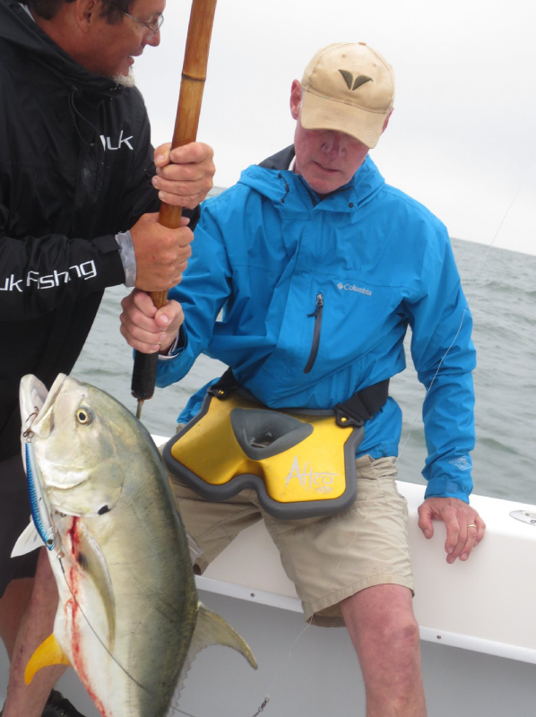 Two men on a boat holding a large fish, with one man pulling the fish by a rope while the other helps.