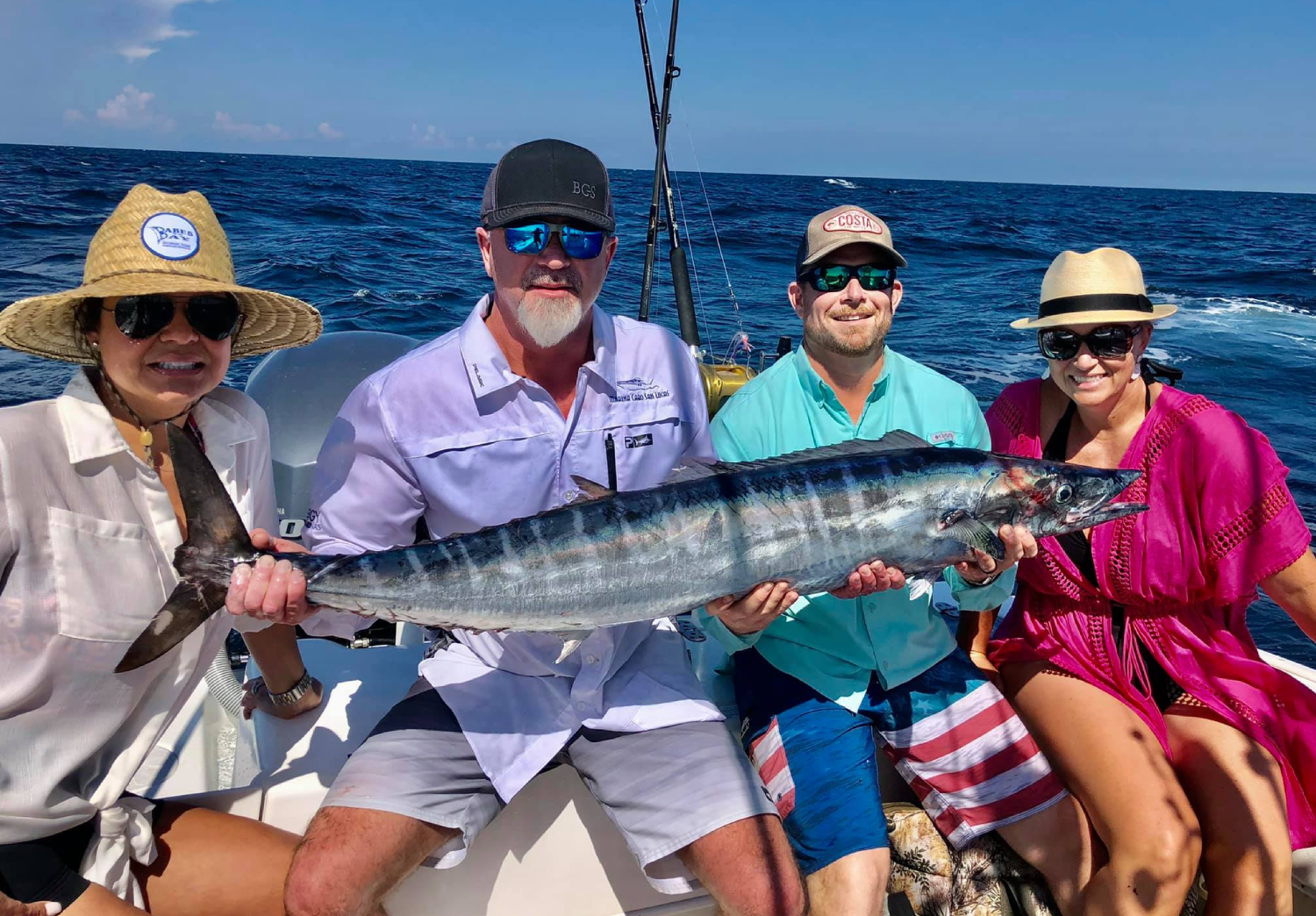 Four people sitting on a boat holding a large fish, with the ocean in the background.