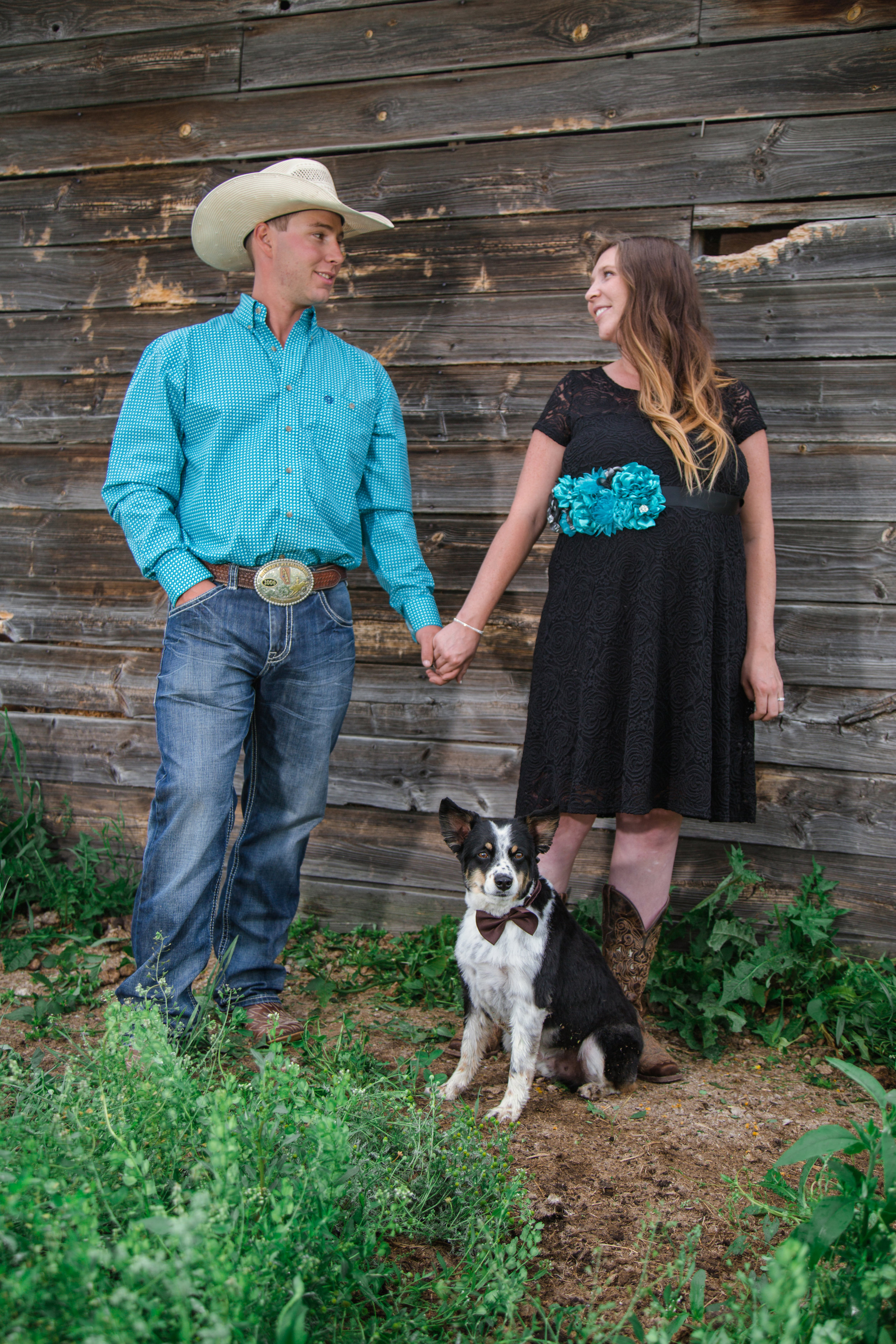  western family maternity photo with barn holding hands with a dog 