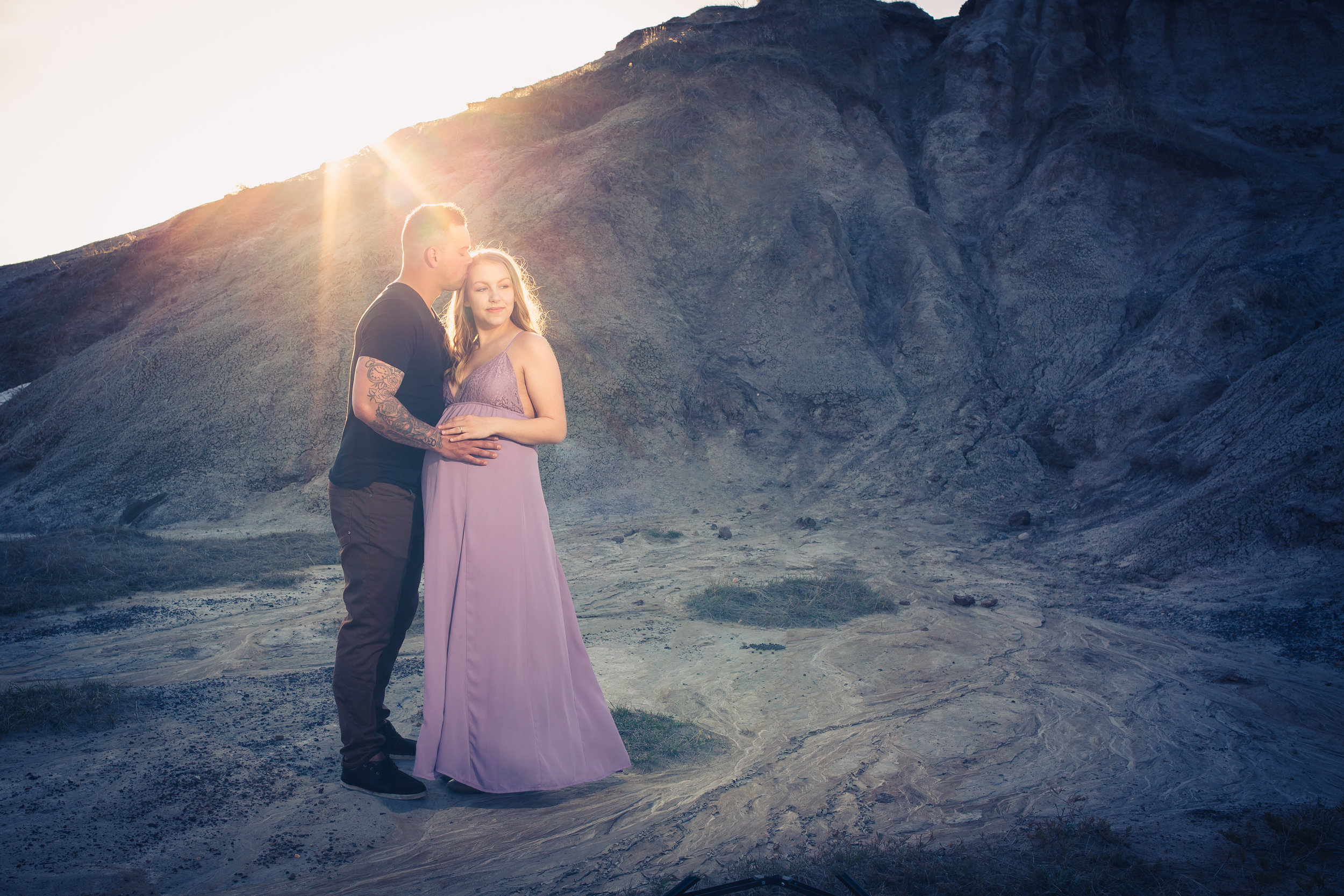 couples maternity holding belly outdoor mountain in a purple dress kissing