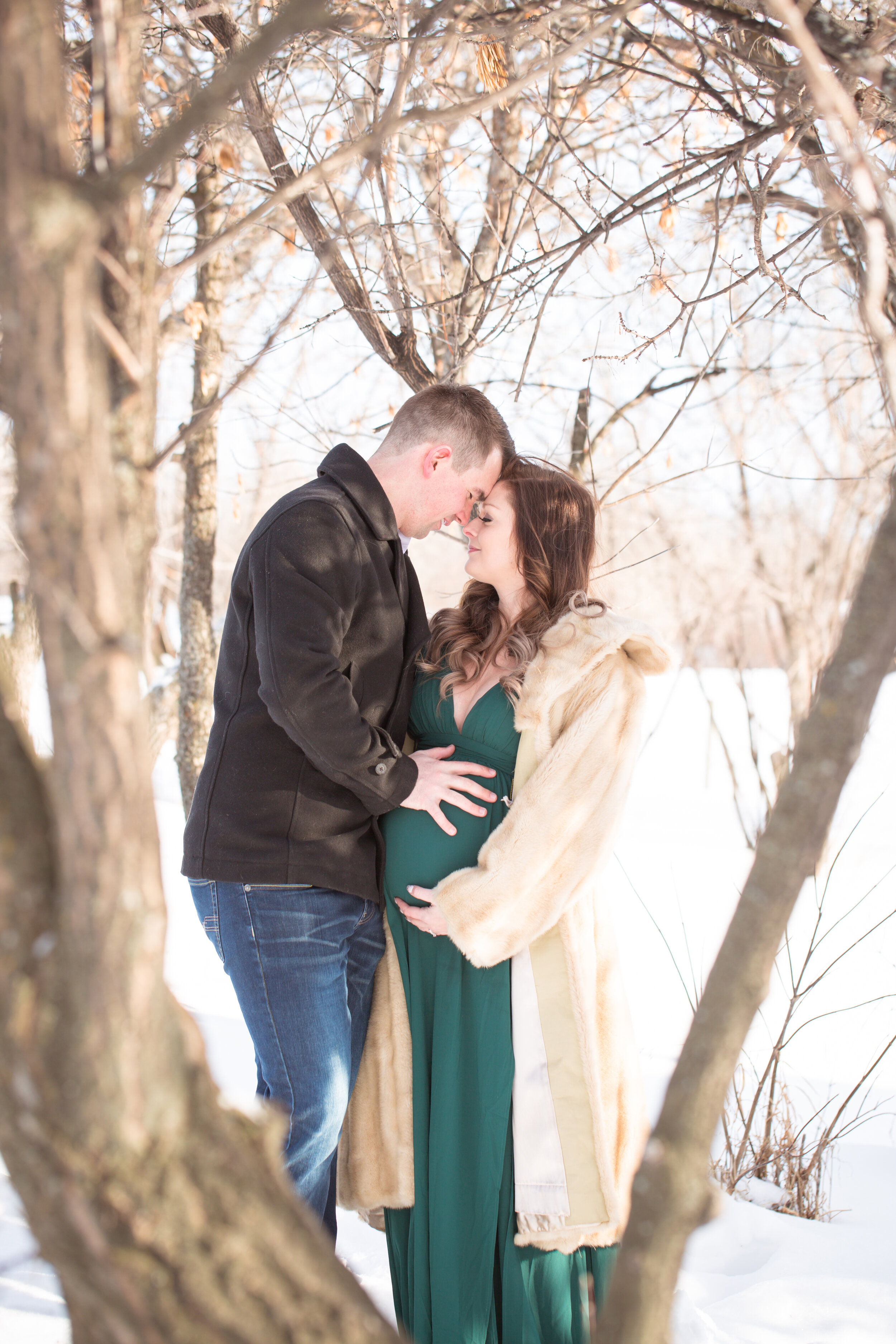 maternity holding belly outdoors in the tree in a green dress