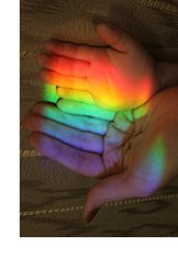 Photograph of the rainbow light of a faceted prism shining over the hands of a mother and child.