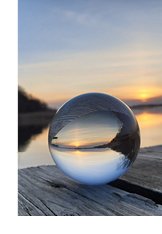 Photograph of a spherical chrystal ball reflecting a hopeful sunset and lakeside landscape.