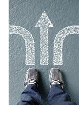 Photograph of view looking down at tennis-shoed feet standing in front of three directional arrows pointing in different directions