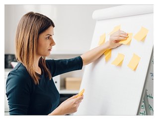 Photograph of young woman adhering yellow post-it notes to an easel-backed paper flip-chart.