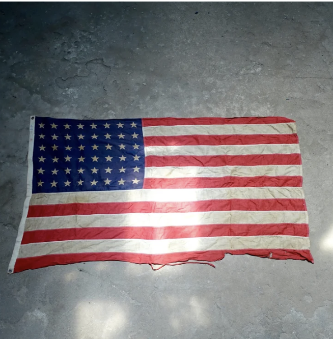 Worn American flag with tears and creases lying on a concrete surface.