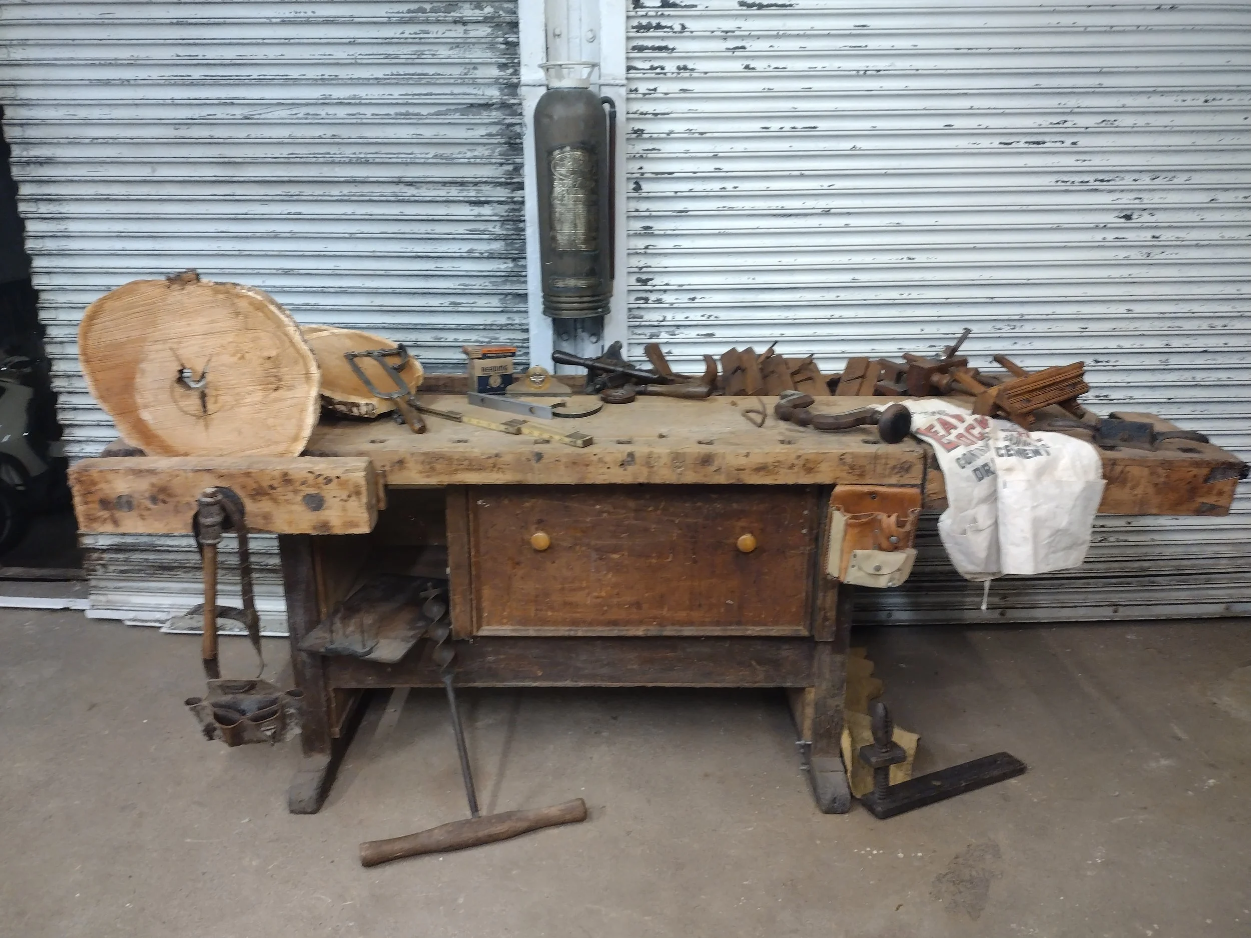 Old wooden workbench with tools and wood scraps in front of a metal garage door.