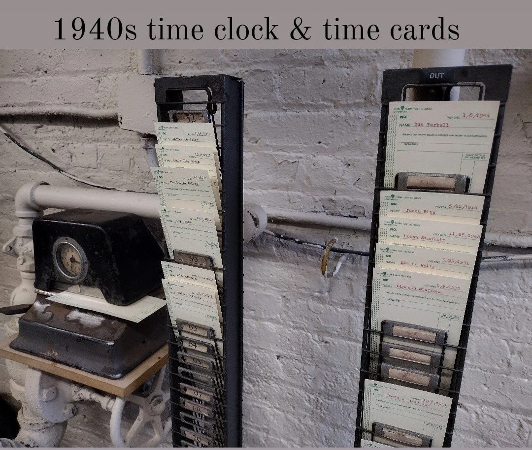 Two vintage 1940s time clocks with time cards hanging, mounted on black metal racks, next to a black and white clock machine against a textured white brick wall.