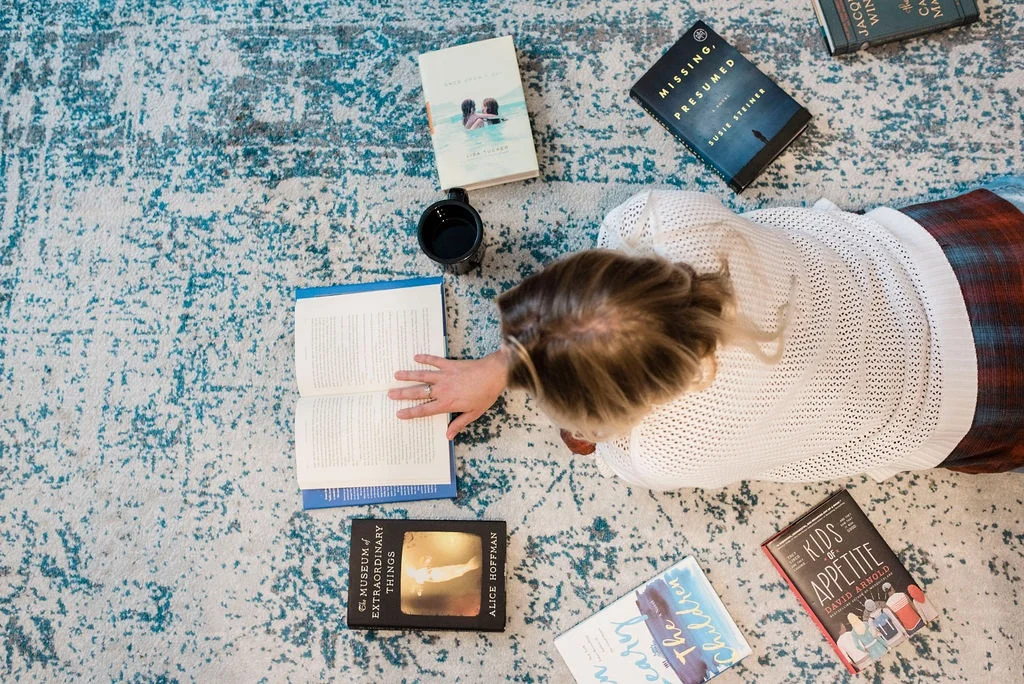 Blonde woman reading while laying on a run surrounded by books