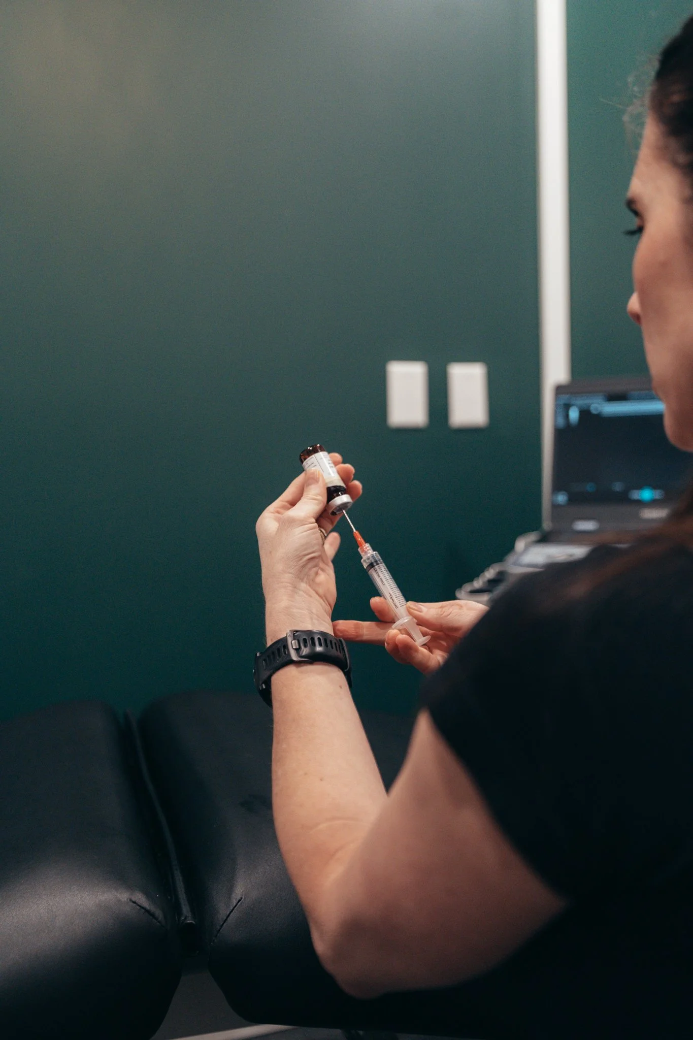 The image is being taken from behind Lorna's head shoulder and you can see her drawing some medicine into a syringe.