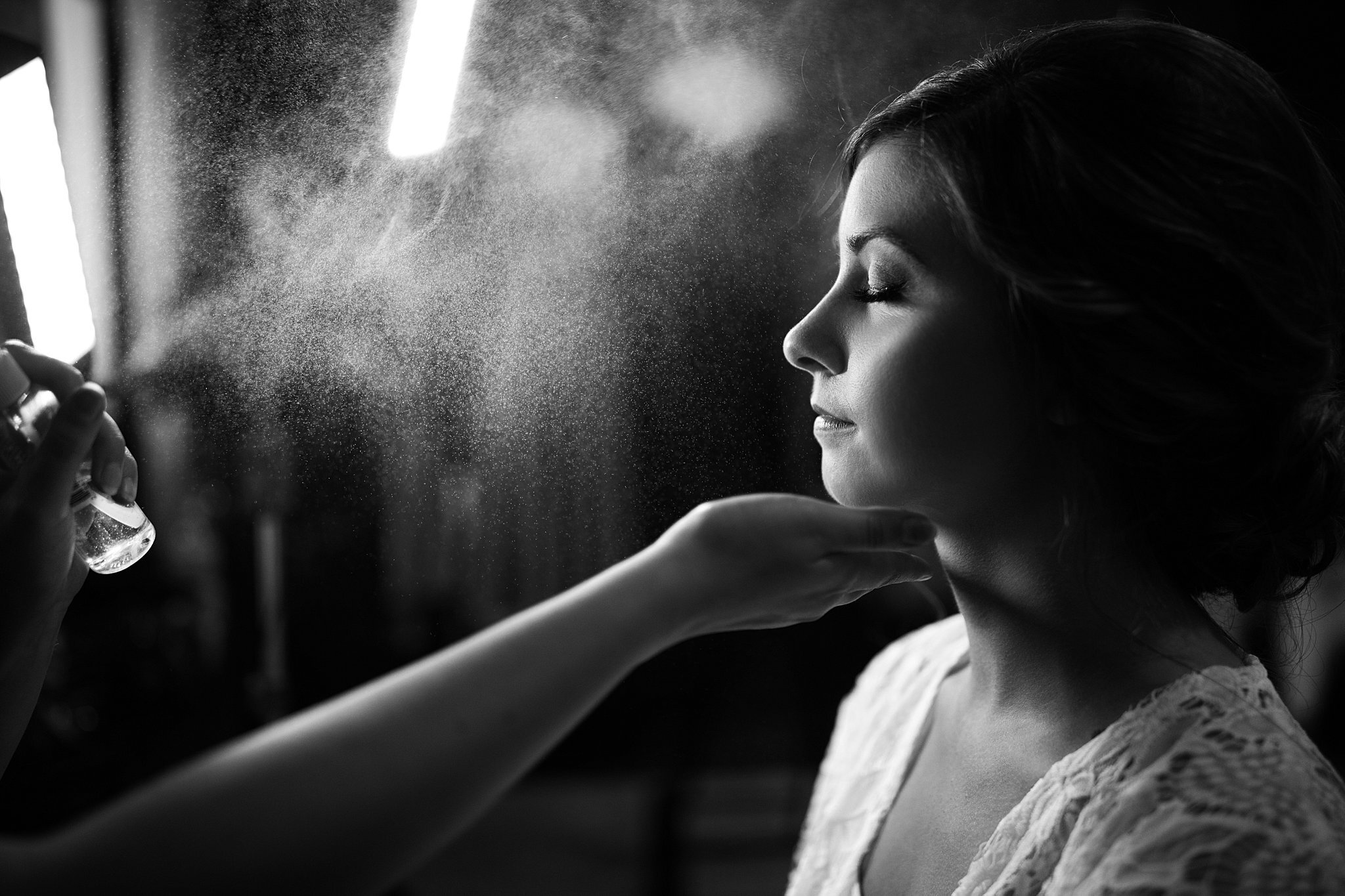  Bride getting spritzed with makeup setting spray by makeup artist. 