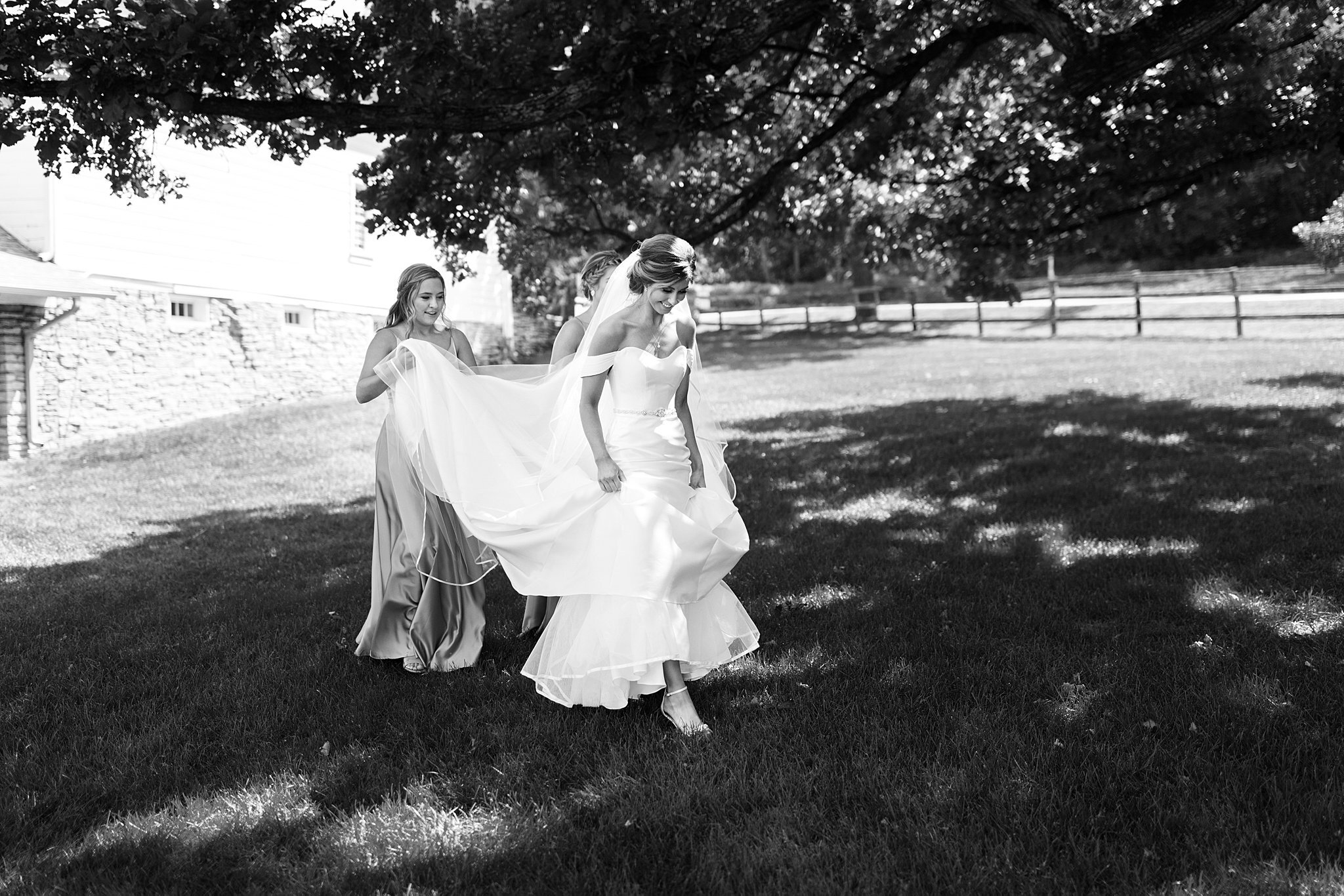  Bridesmaids carrying brides train outside Mayowood Stone Barn. 