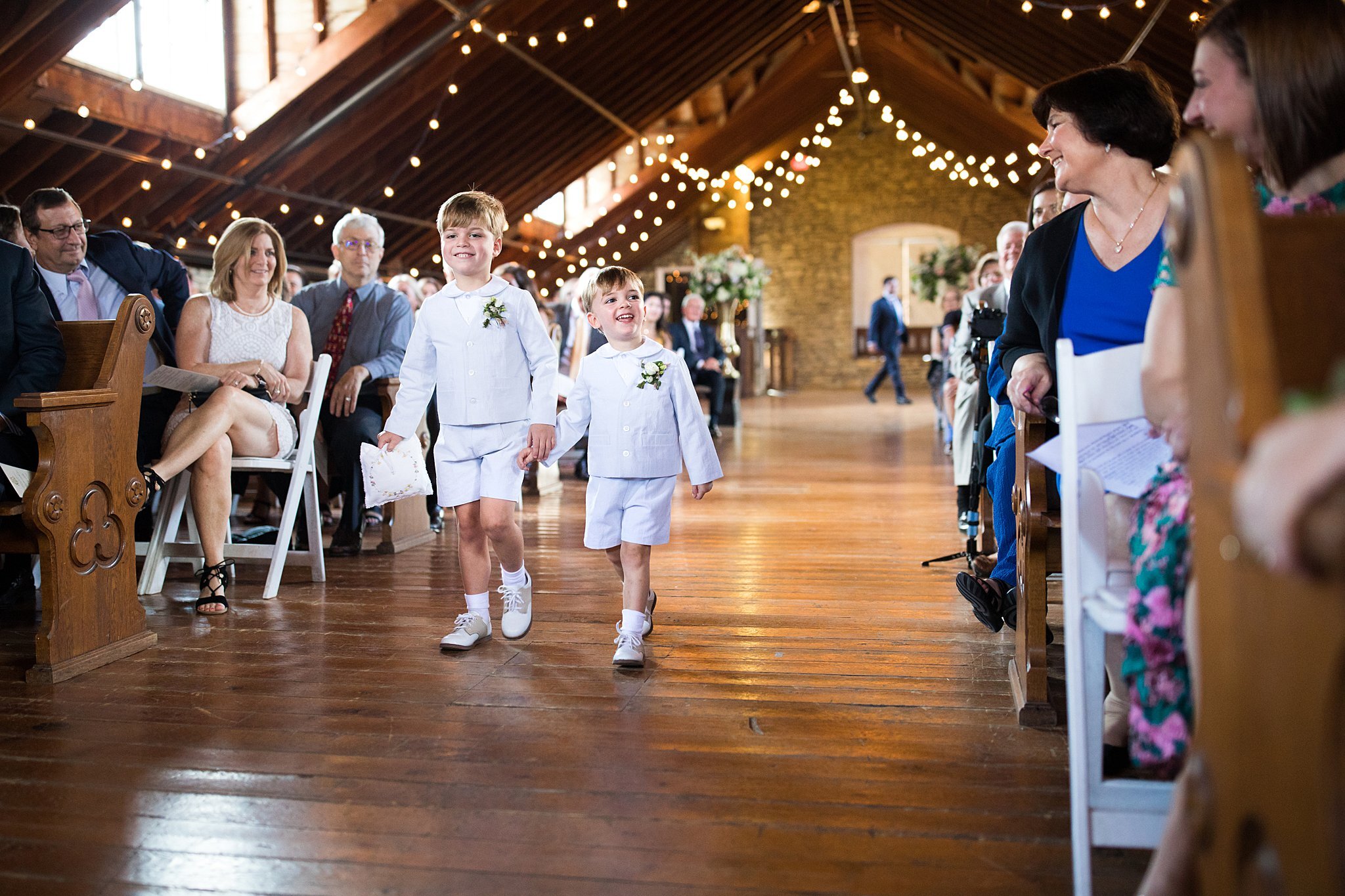  Two ring bearer boys holding hands and walking down the aisle. 