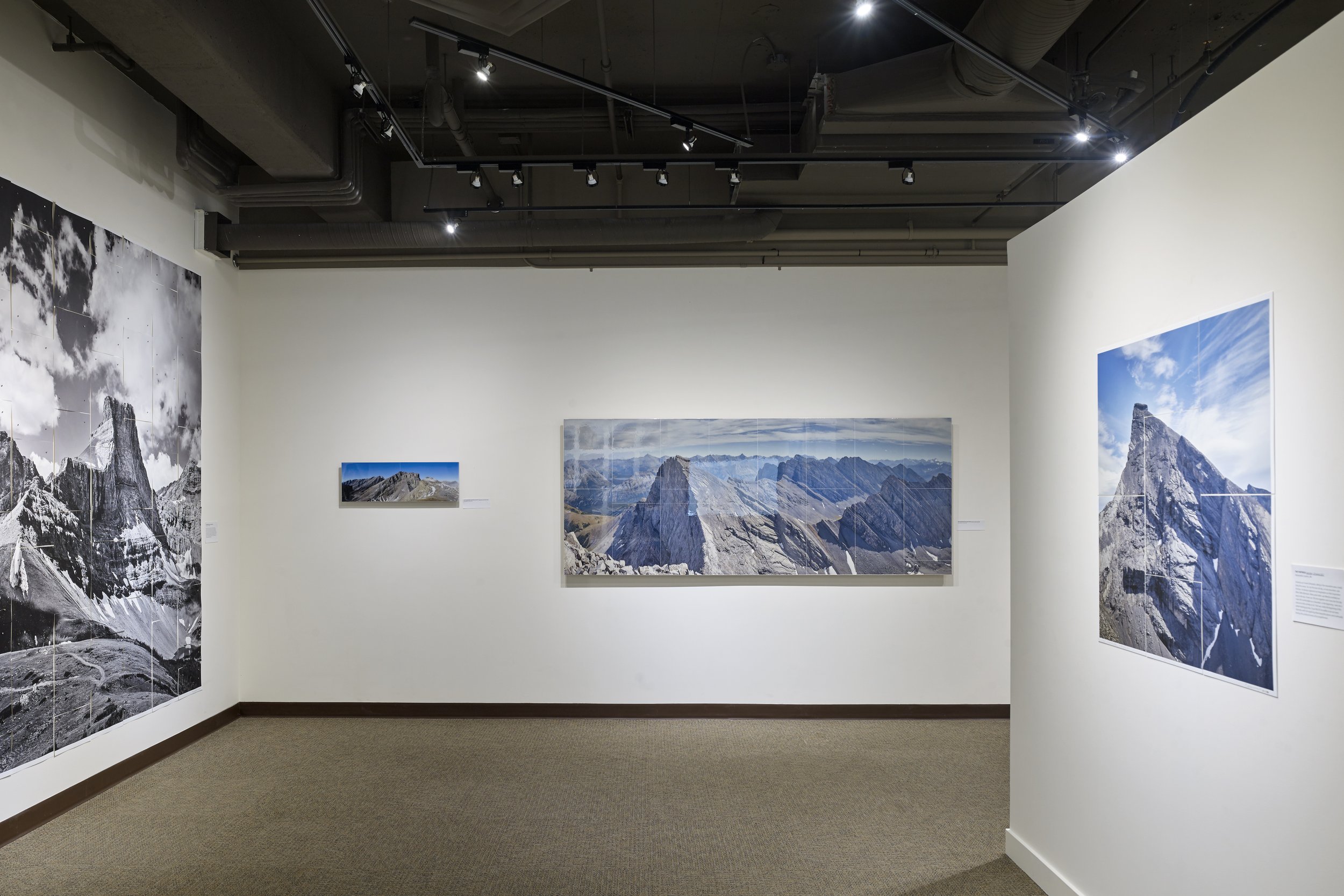   UPHIGH , Canmore Museum, 2024. Left image:  Little Fortress  2023. 10” x 30”, tiled photographs on hardboard with epoxy resin. Right image:  The Fortress (from Gusty Peak)  2021. 39” x 97”, tiled photographs on hardboard with epoxy resin. 