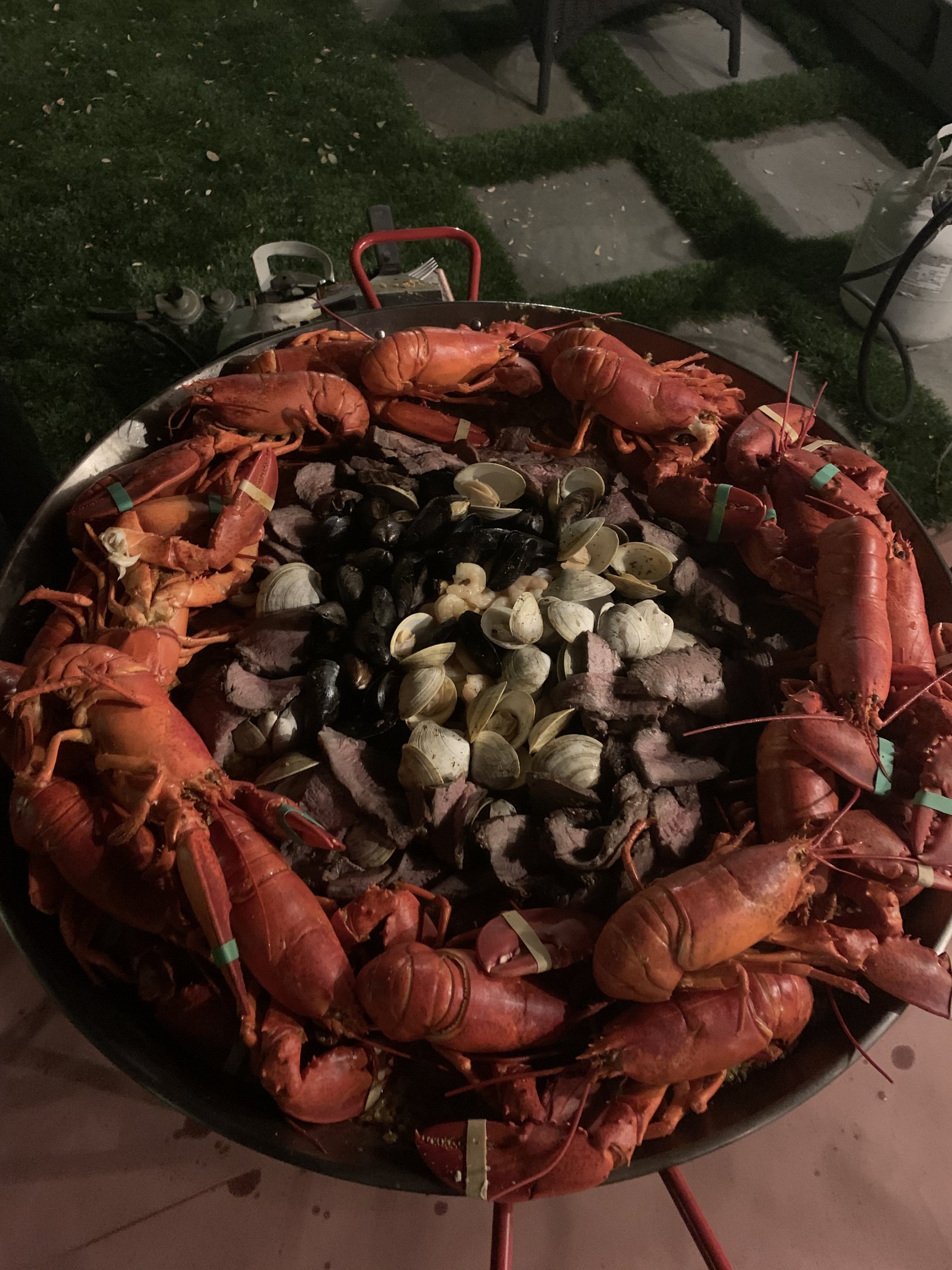 Special occasion celebration dinner. Paella with chicken, chorizo, topped with prawns, clams, mussels, thin slices of grilled tri tip, and steamed whole live lobsters.