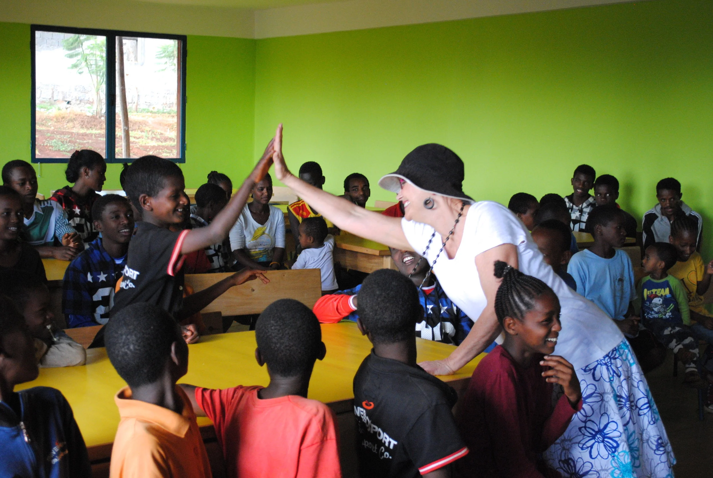 Val Easton, a volunteer for Mothers with a Heart for Ethiopia, gives a high-five to a child in the Busajo program in Soddo, Ethiopia after doing a fun singalong with the kids. 