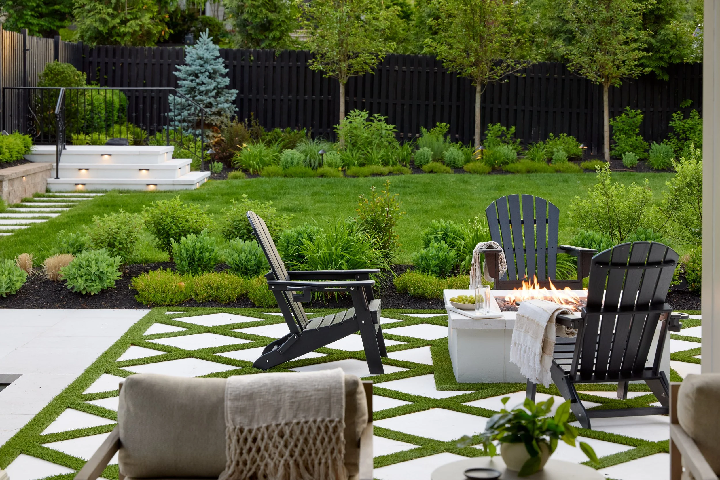 Custom fire-pit patio in NJ with large-format geometric pavers, grass joints, Adirondack seating and layered backyard landscaping.jpg