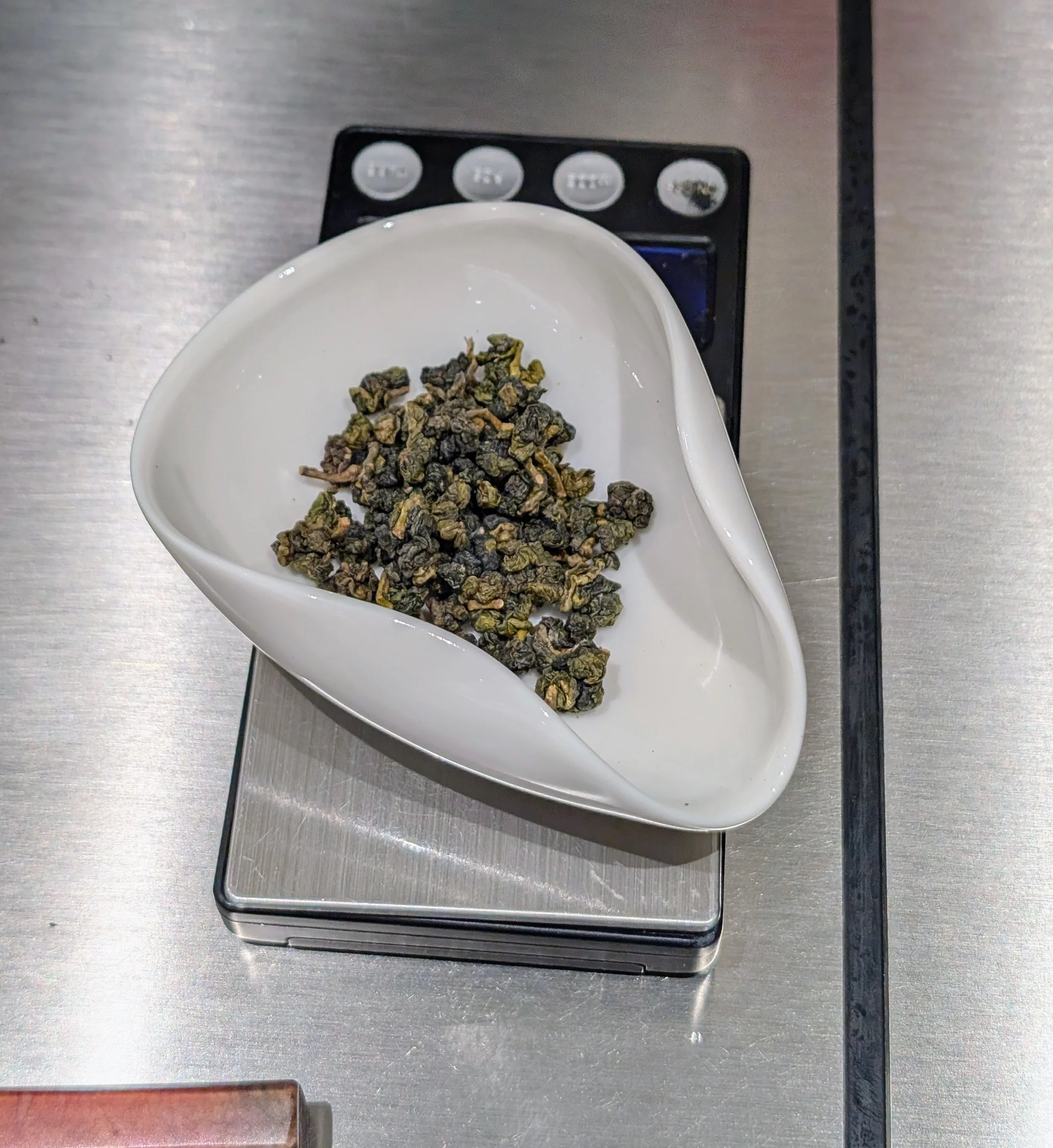 Oolong tea leaves in a curved tray on a scale. The background is a stainless steel counter