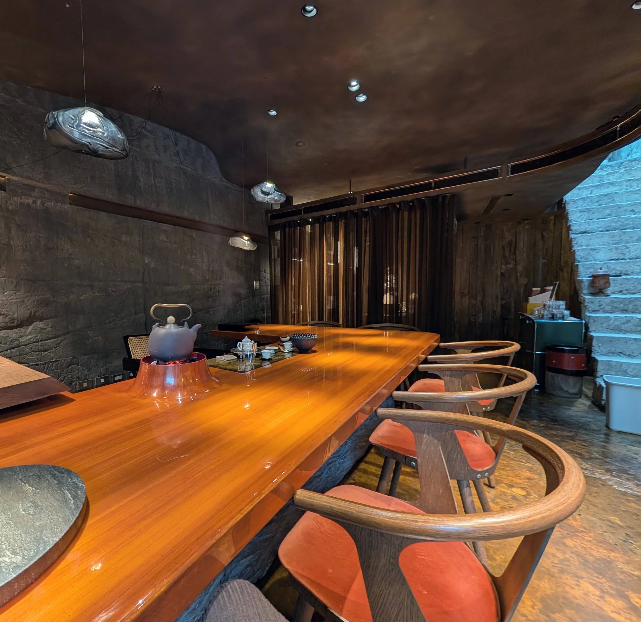 Tea tasting counter at Liquid Ambre, a wooden u shaped counter with chairs and on the other side a tea brewing station for the host with a kettle, a tea pot, pitcher and tea cups