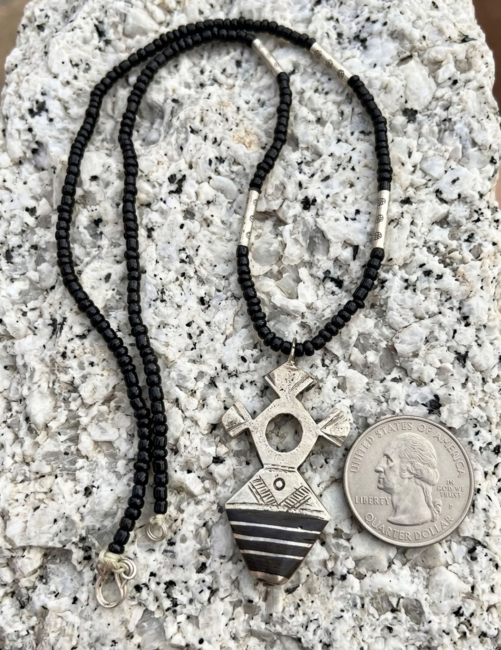 Handcrafted Moroccan Tuareg Cross pendant necklace with ebony wood inlay, black bead strand, and quarter shown for size comparison.