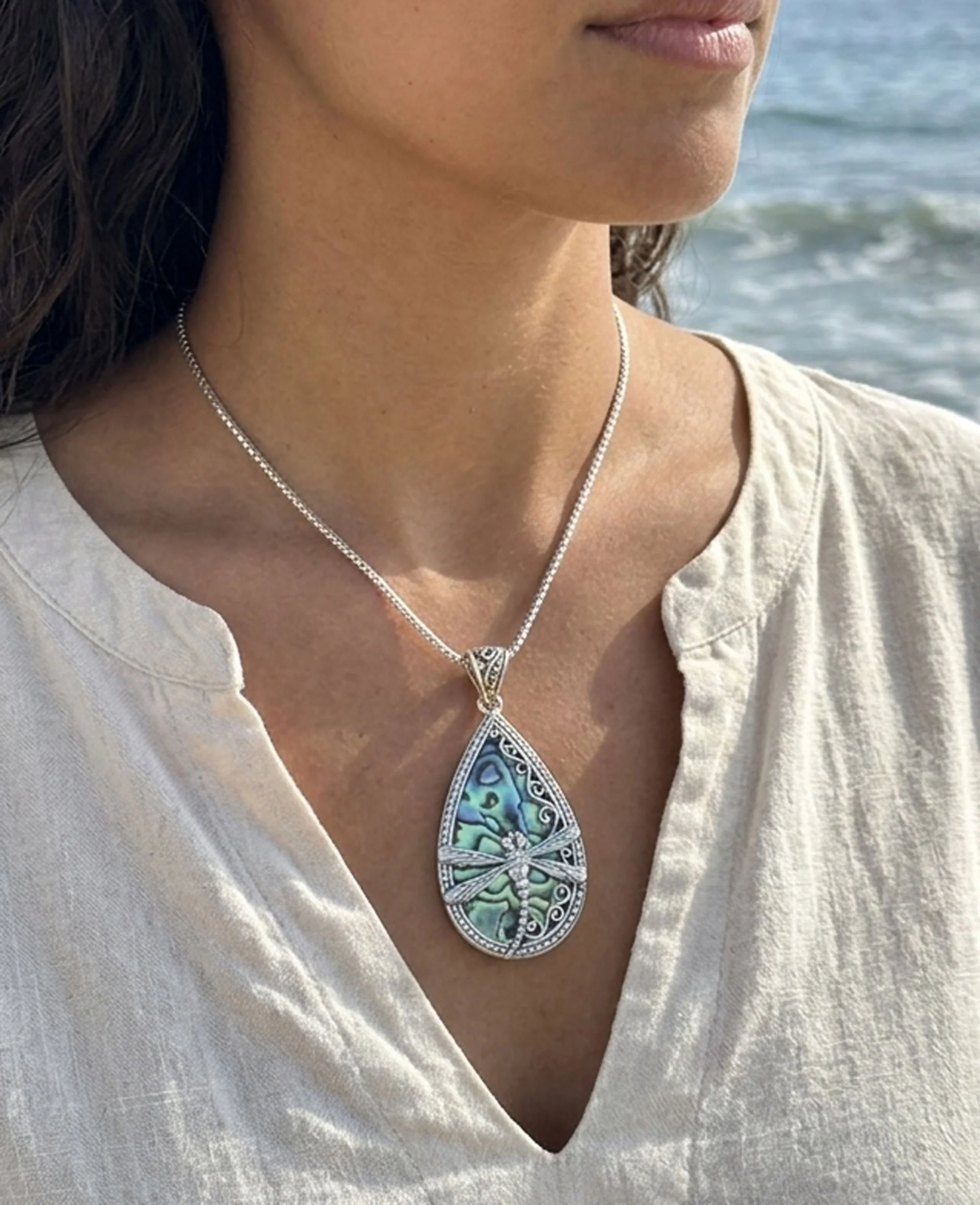 Woman wearing sterling silver dragonfly pendant with shimmering abalone shell on a silver chain.
