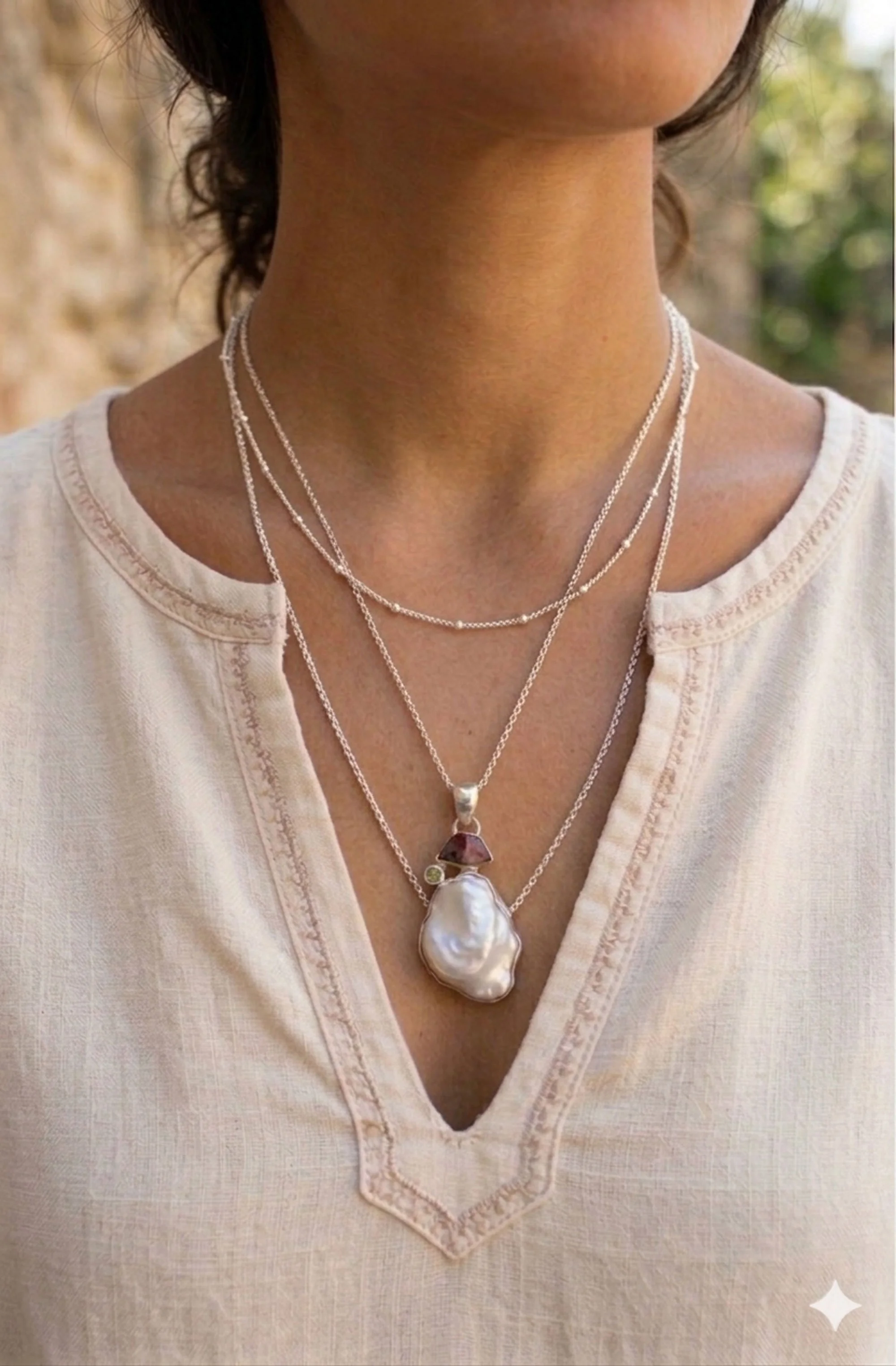 Baroque pearl and tourmaline sterling silver pendant necklace held by model, gemstone jewelry shown as a layered look