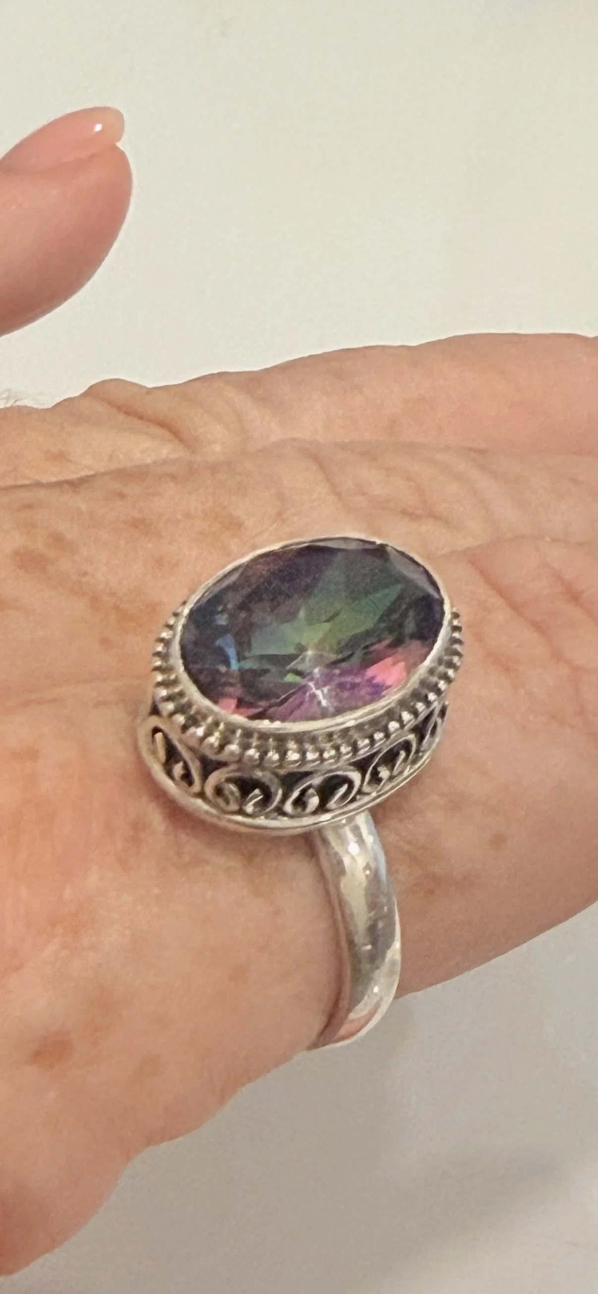 Mystic Topaz size 10 ring worn on hand showing oval iridescent gemstone and sterling silver band.