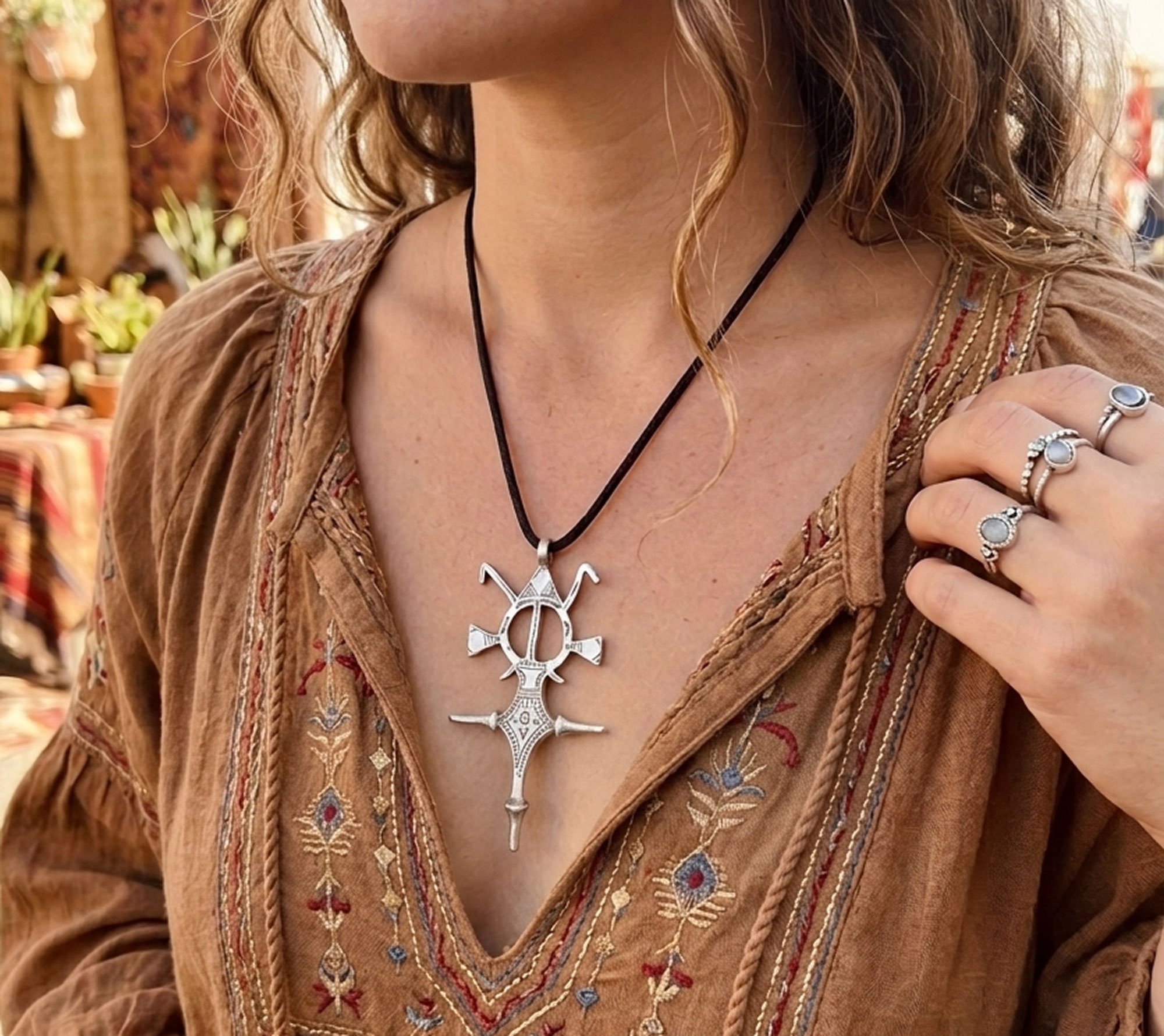 Woman wearing a handcrafted Moroccan Tuareg cross pendant necklace in silver on a black cord. Boho tribal jewelry inspired by North African nomadic design and artisan craftsmanship.