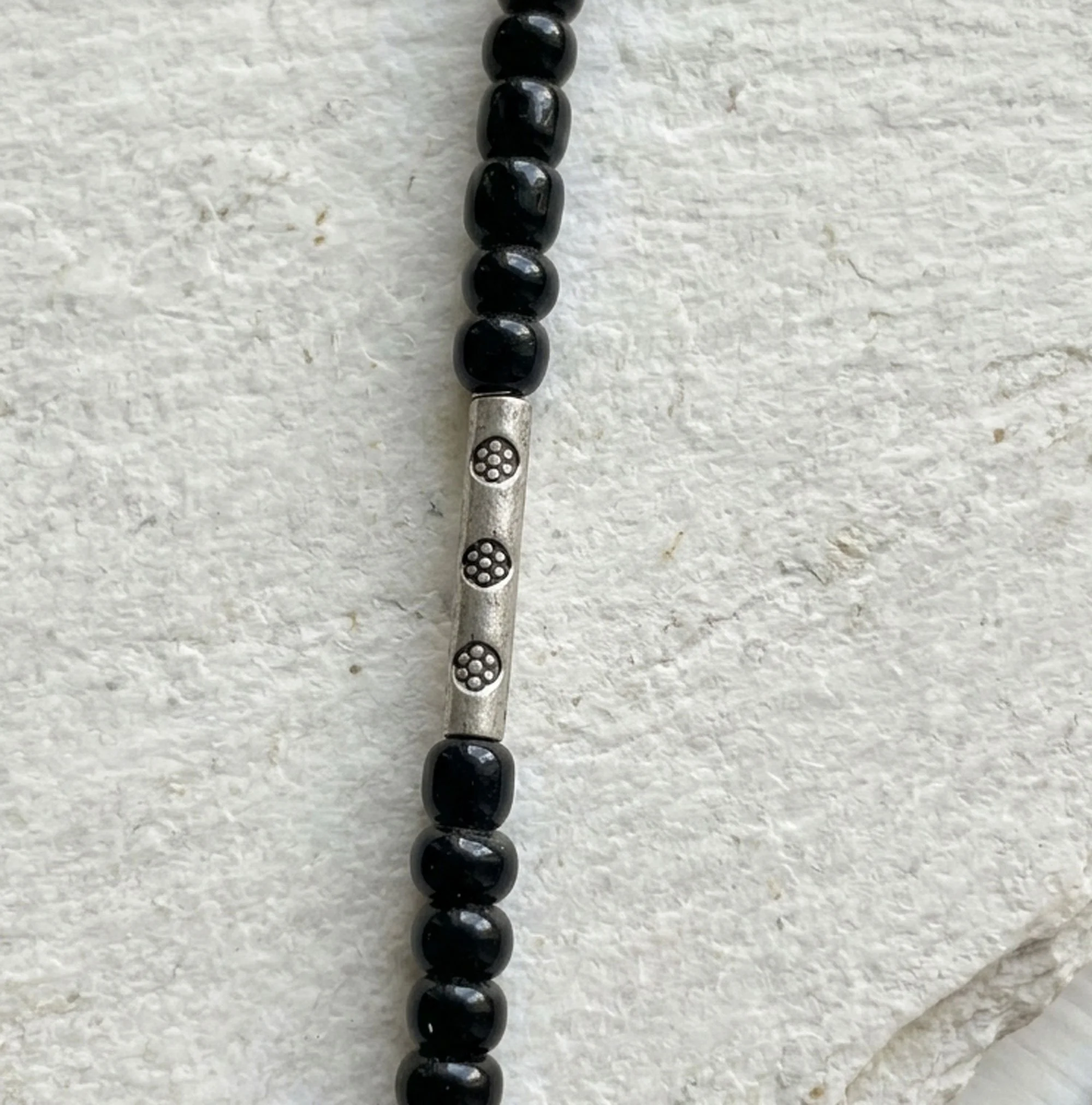 Close-up of decorative silver tribal bead and black glass seed beads on Moroccan-inspired necklace.