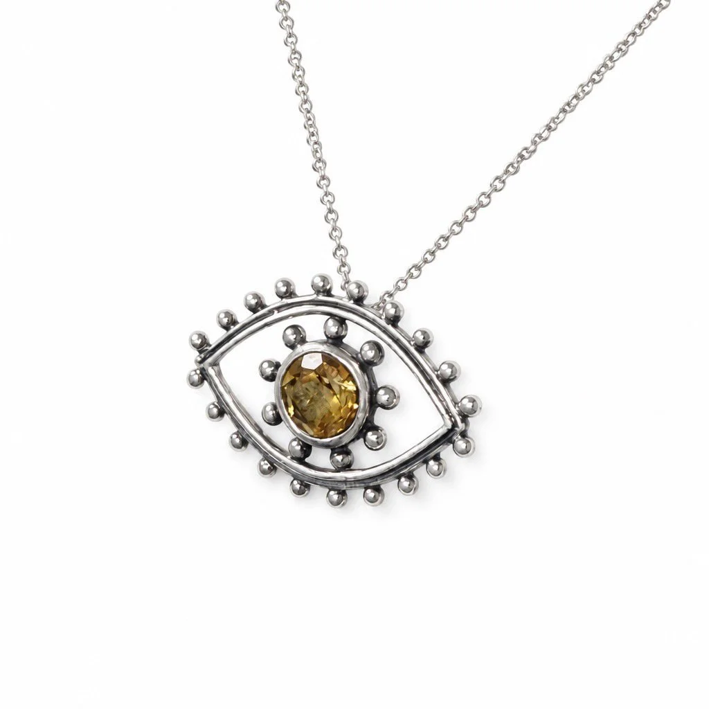 Close-up of a golden citrine gemstone set in a sterling silver Evil Eye pendant on a white background.