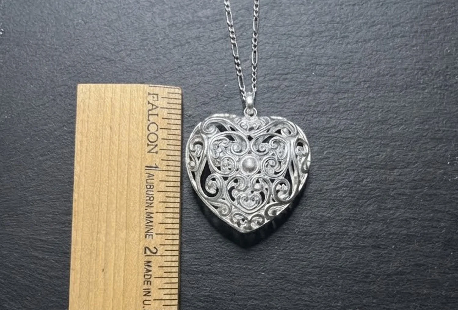 Large sterling silver heart pendant with scroll design shown beside a ruler for scale