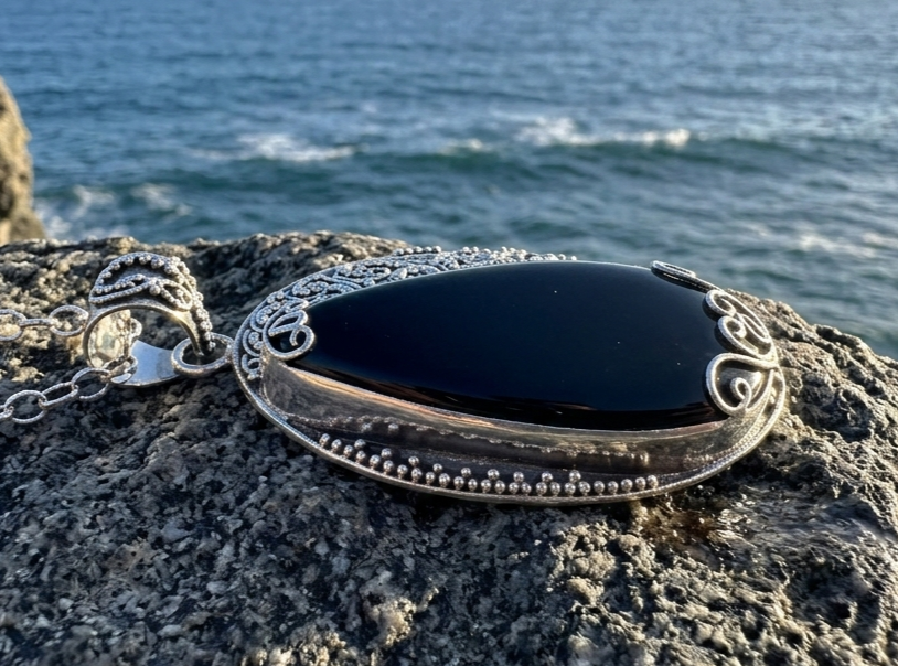 Handcrafted sterling silver pendant featuring a polished black onyx stone with ornate filigree metalwork,