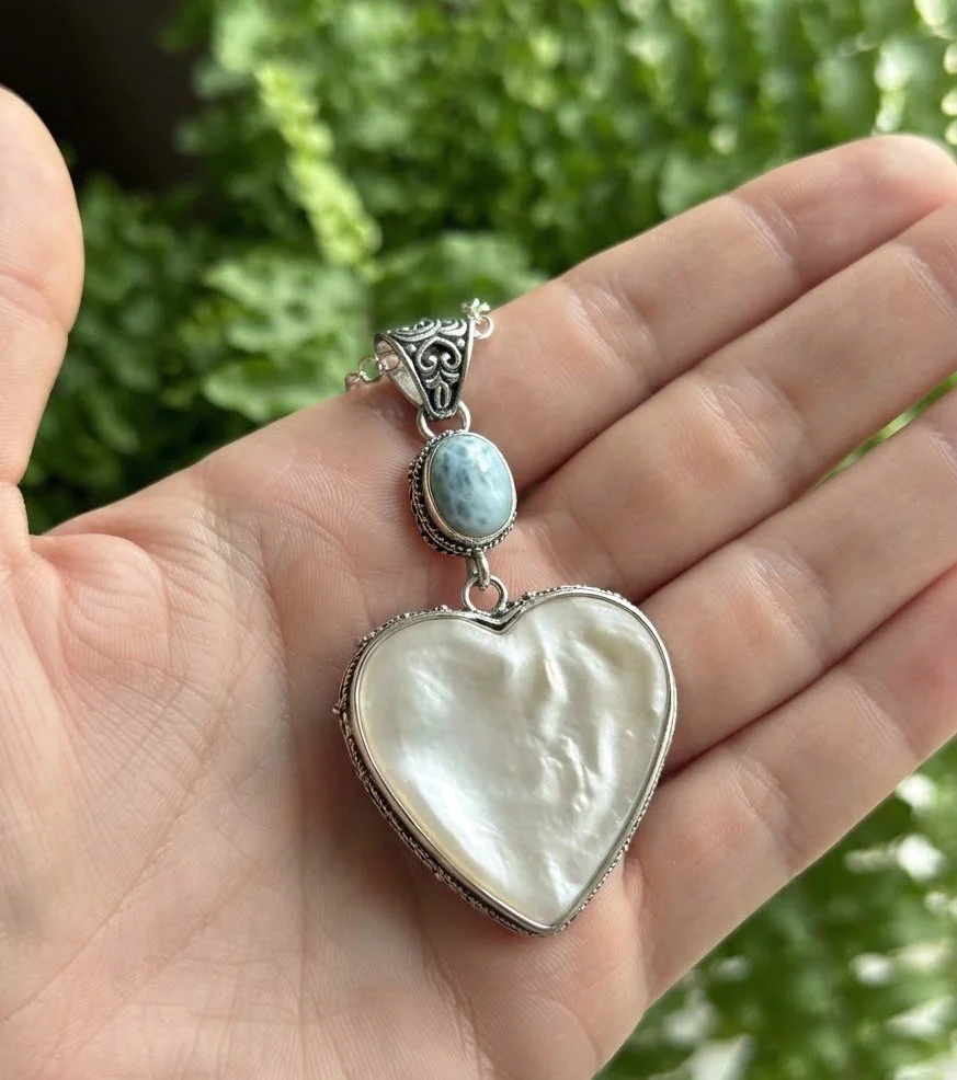 Mother of Pearl heart pendant with blue Larimar and sterling silver shown in hand for scale