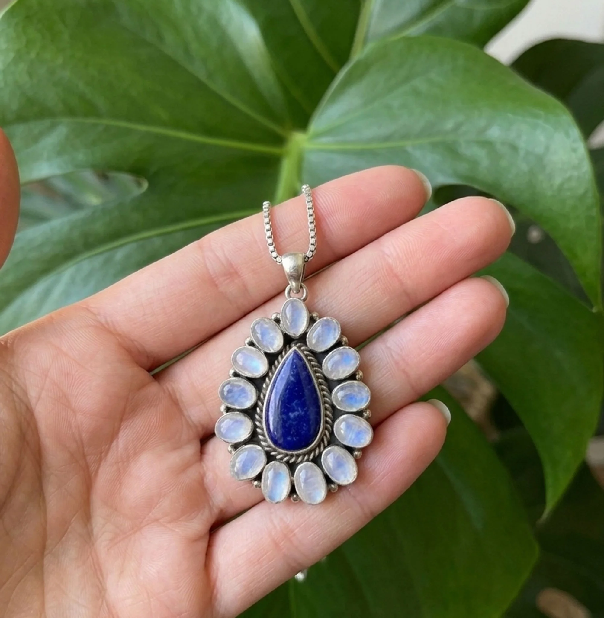 Handcrafted sterling silver pendant featuring a pear-shaped genuine Lapis Lazuli gemstone surrounded by twelve glowing Rainbow Moonstones with blue flash, artisan-made