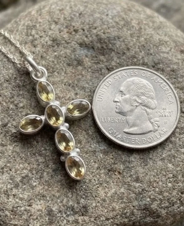 Citrine cross pendant with six oval golden gemstones set in sterling silver, shown next to quarter for scale