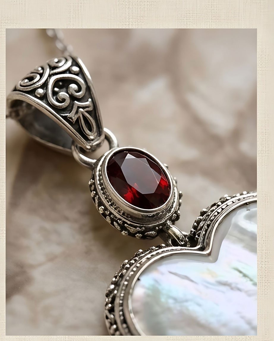 Close-up of faceted red garnet, sterling silver scrollwork bail, and mother of pearl heart