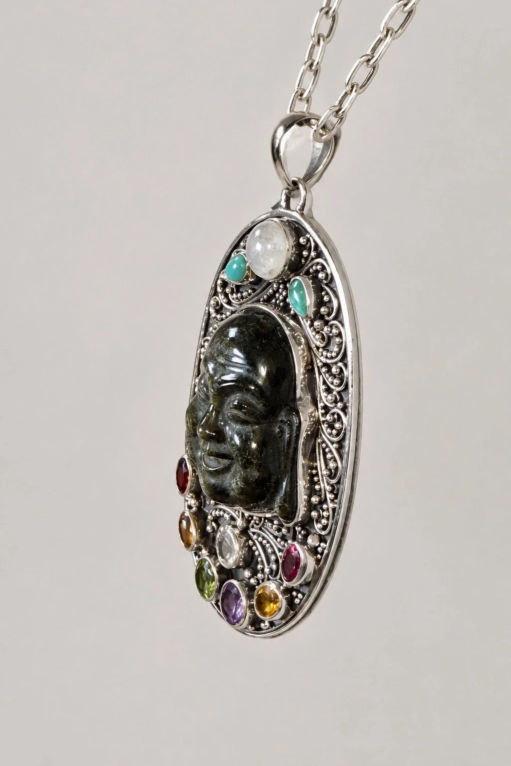 Side view of carved obsidian Buddha pendant showing raised carving and silver setting