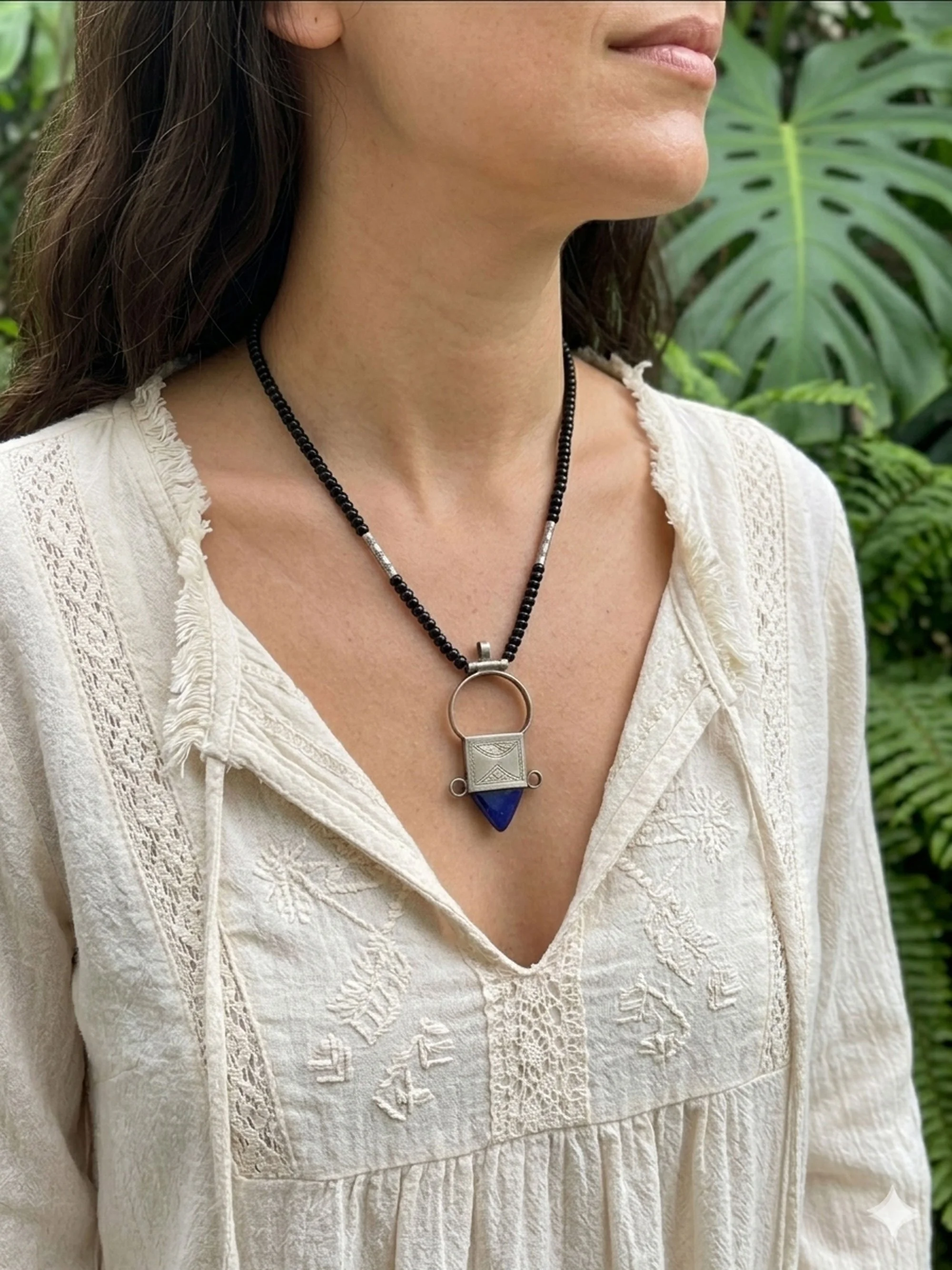 Woman wearing a Moroccan-inspired blue stone tribal pendant necklace on a black beaded strand.
