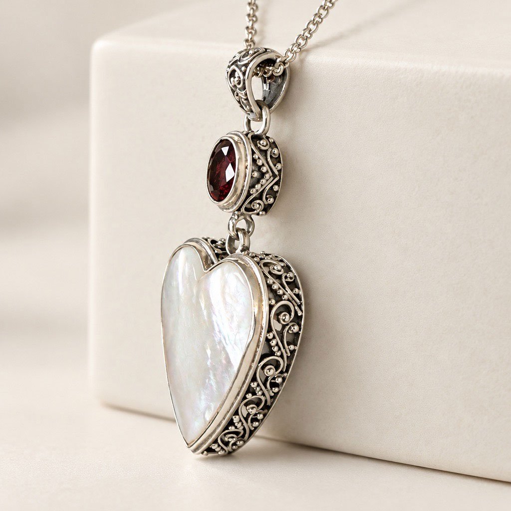 Side view of mother of pearl and garnet heart pendant showing detailed sterling silver scrollwork