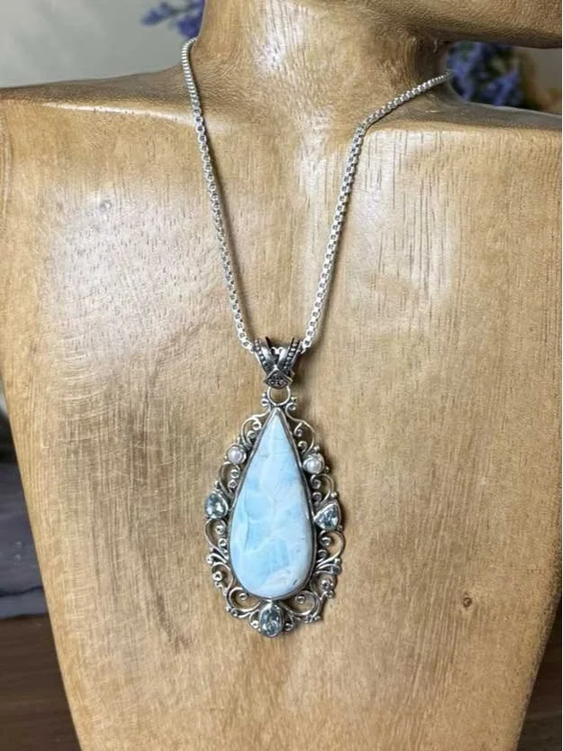 "Handcrafted sterling silver Larimar pendant with teardrop gemstone, accented by blue topaz and freshwater pearls on an ornate chain.
