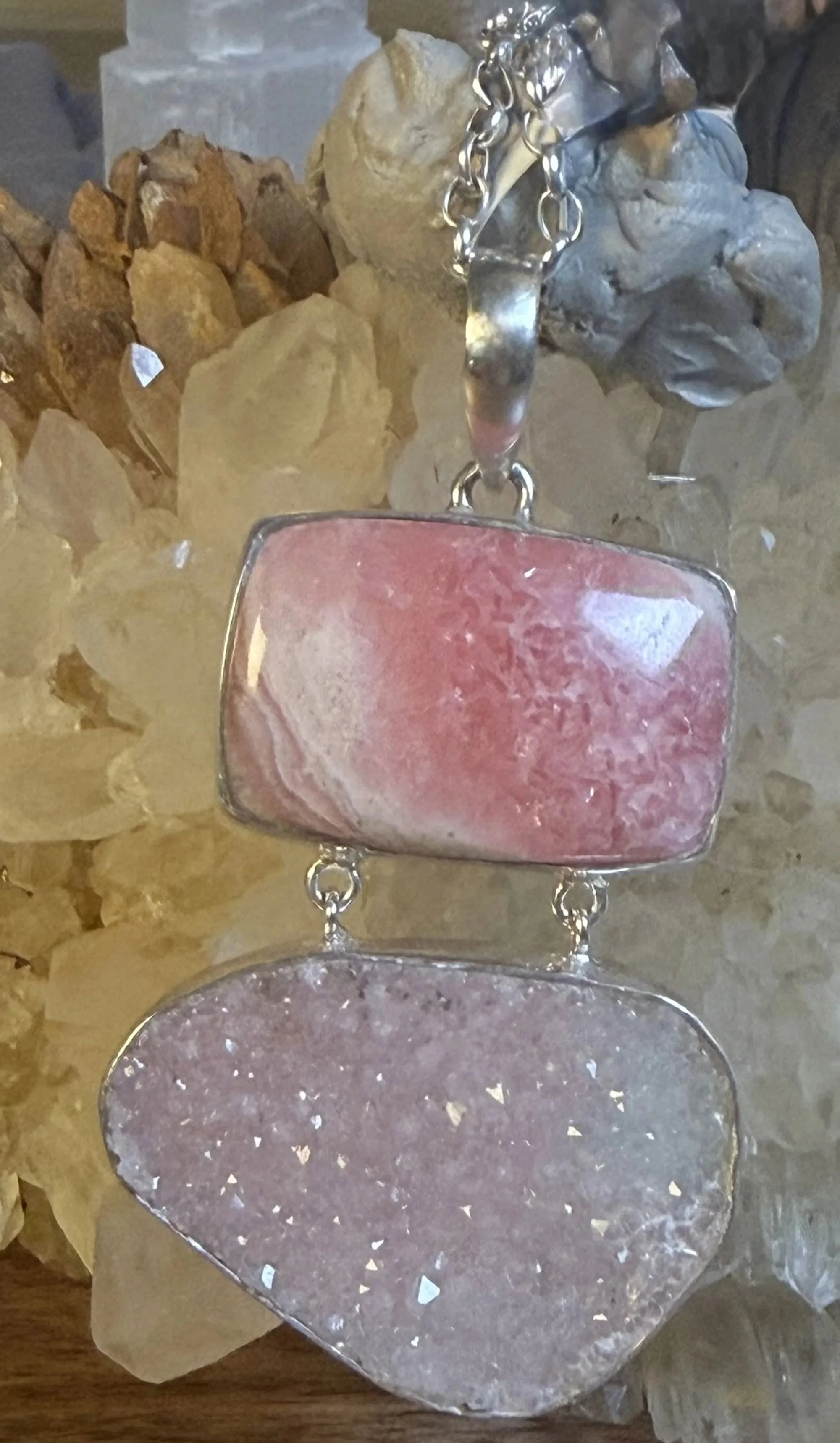 Close-up of pink rhodochrosite and druzy pendant displayed with natural crystals