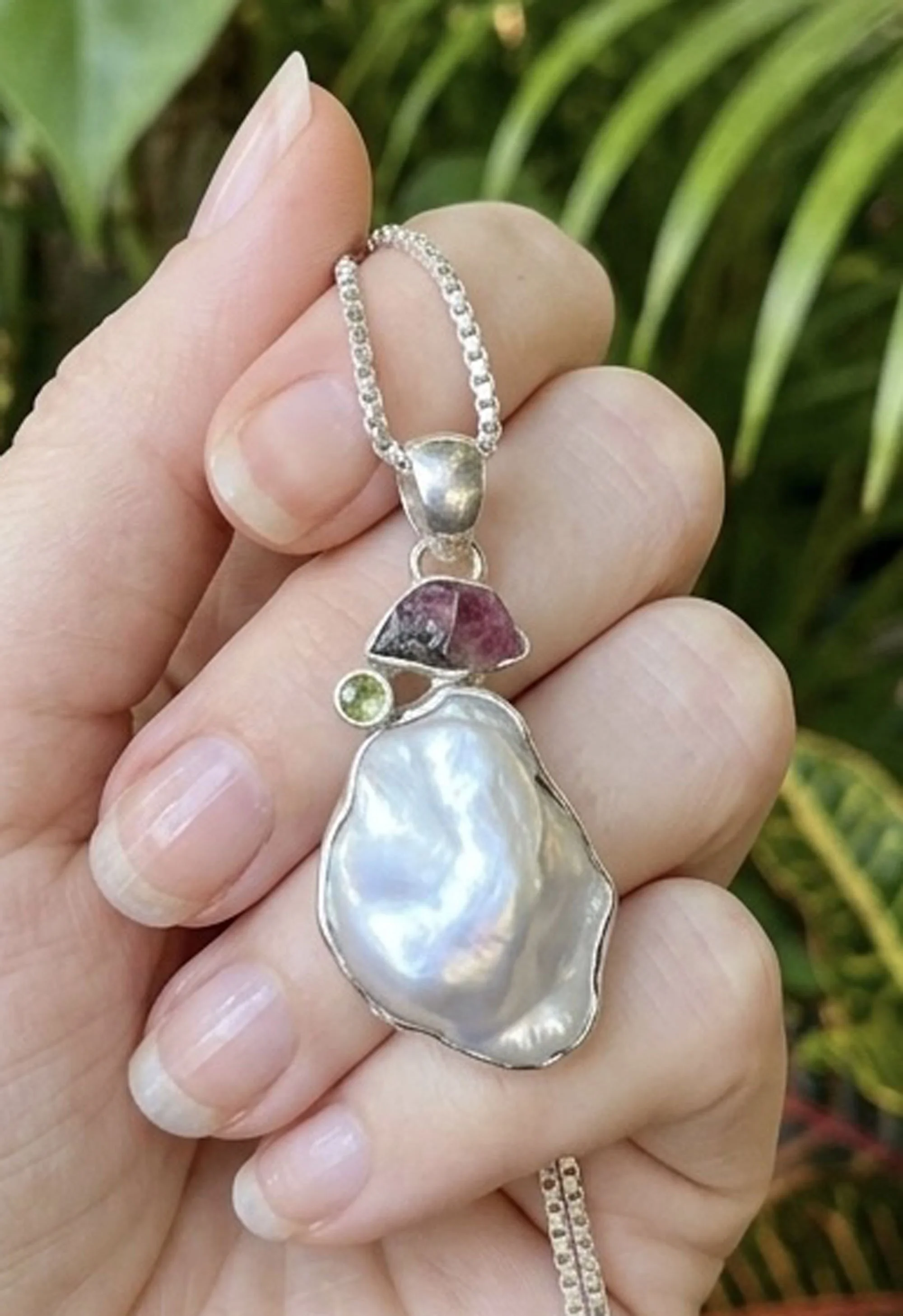 Baroque pearl and tourmaline sterling silver pendant necklace held by model, gemstone jewelry