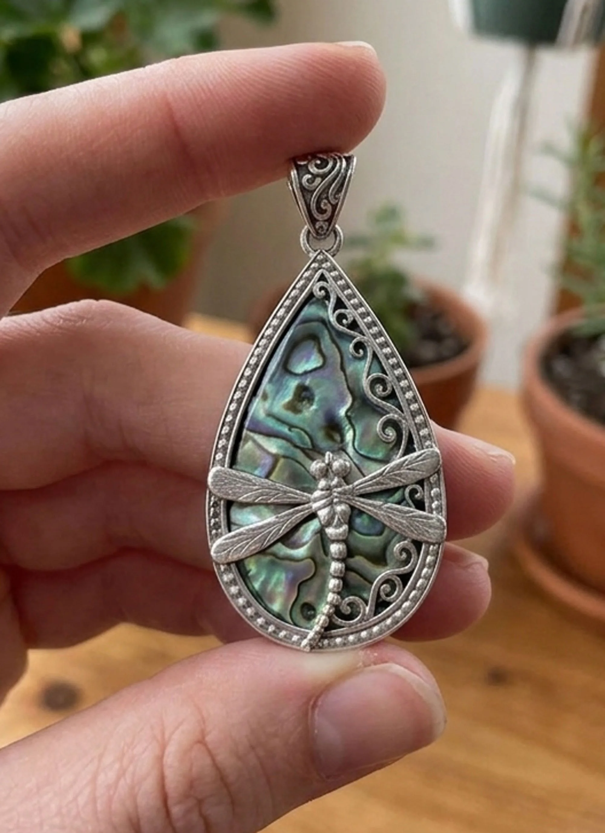 Close-up of handcrafted sterling silver dragonfly pendant with iridescent abalone shell held in hand.