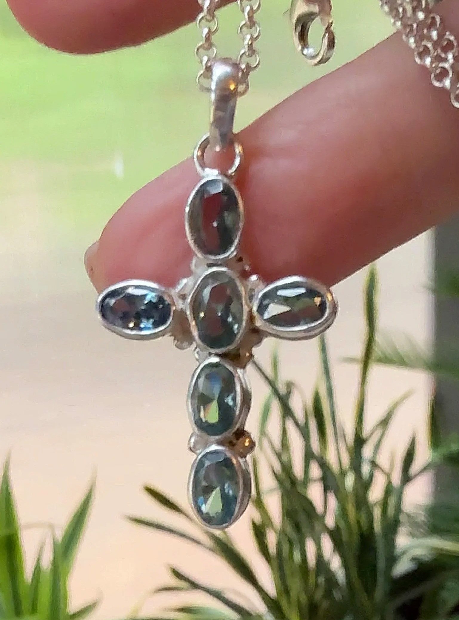 Handheld view of Blue Topaz Cross Pendant with six faceted gemstones set in sterling silver