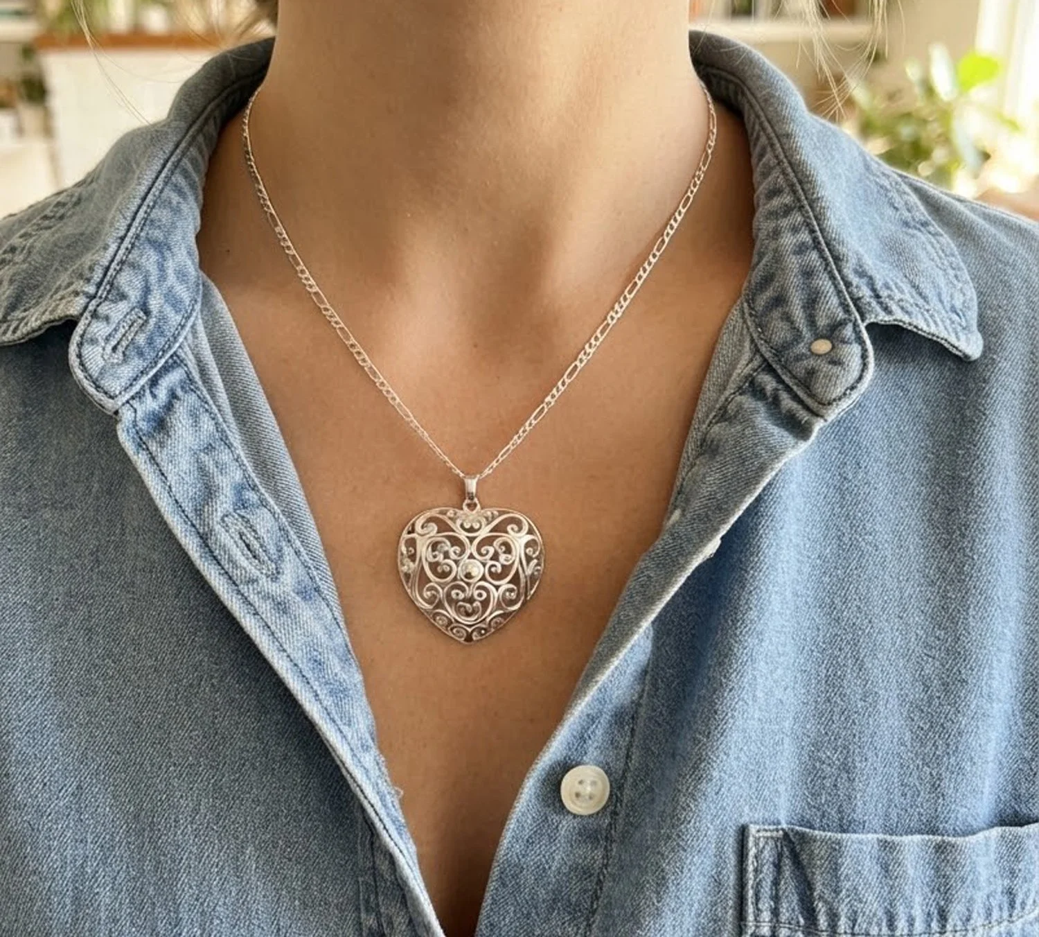 Large sterling silver openwork heart pendant worn on a chain with a denim shirt